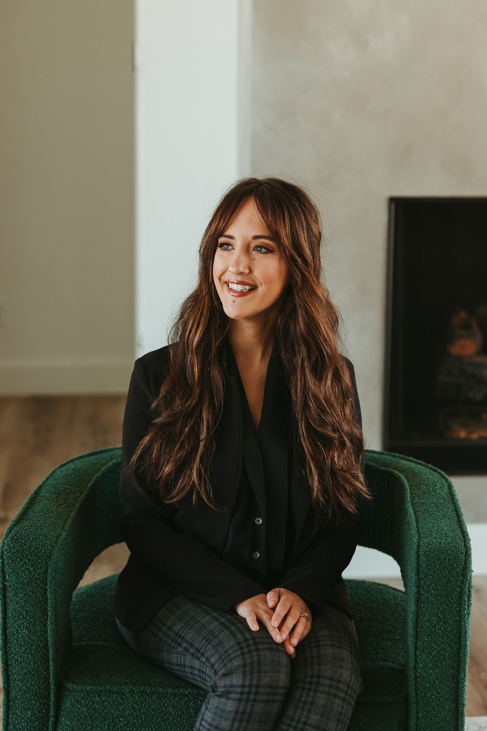 Woman smiling in a green armchair in a modern living room with a fireplace.