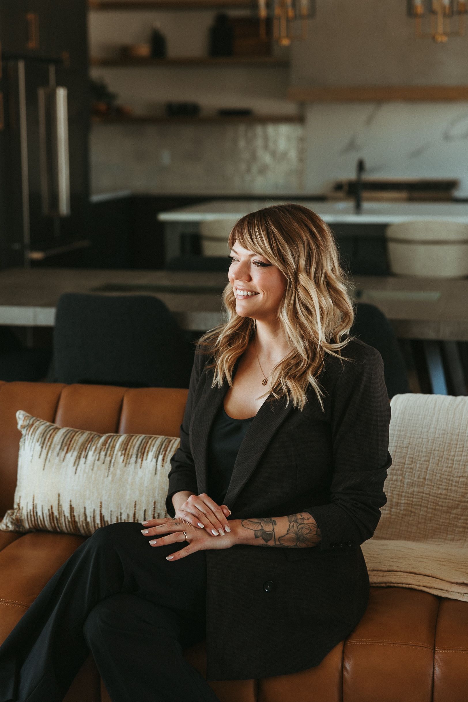 Woman seated on a tan couch in a modern living room, smiling and looking to the side