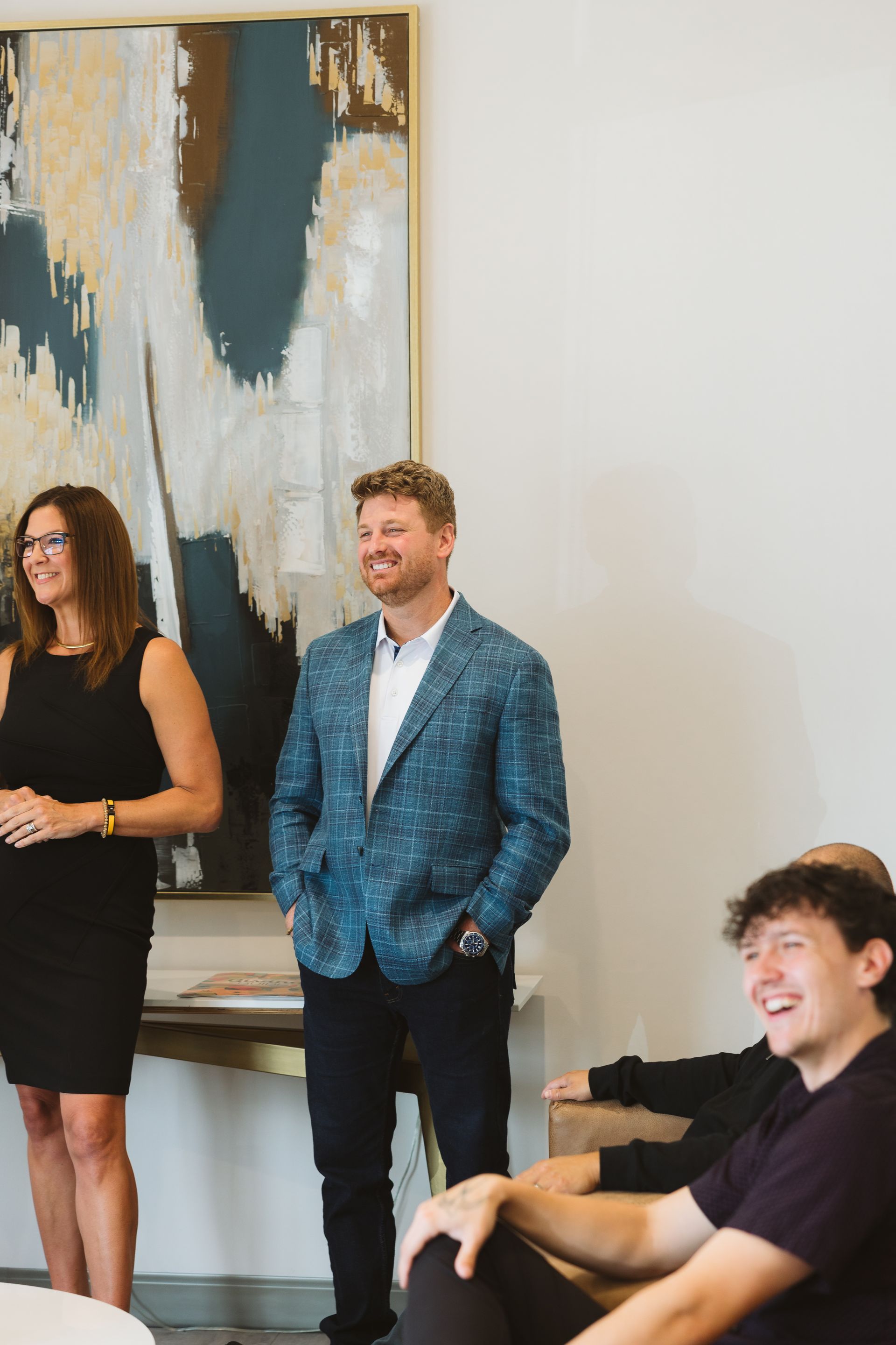 People standing in a modern room, with an abstract painting on the wall and one person seated in front.