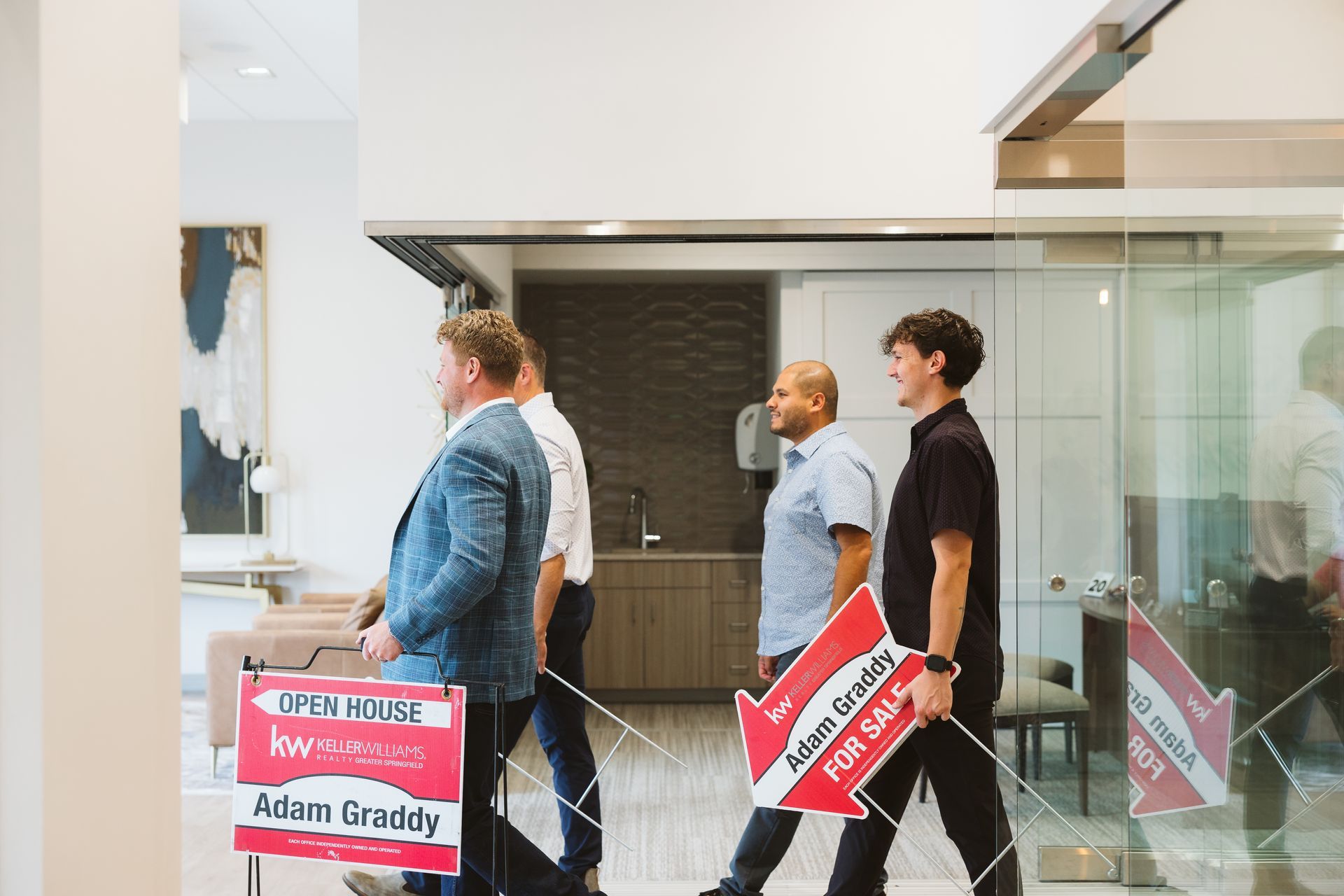 Three people walking indoors past glass walls, two carrying red-and-white signs.