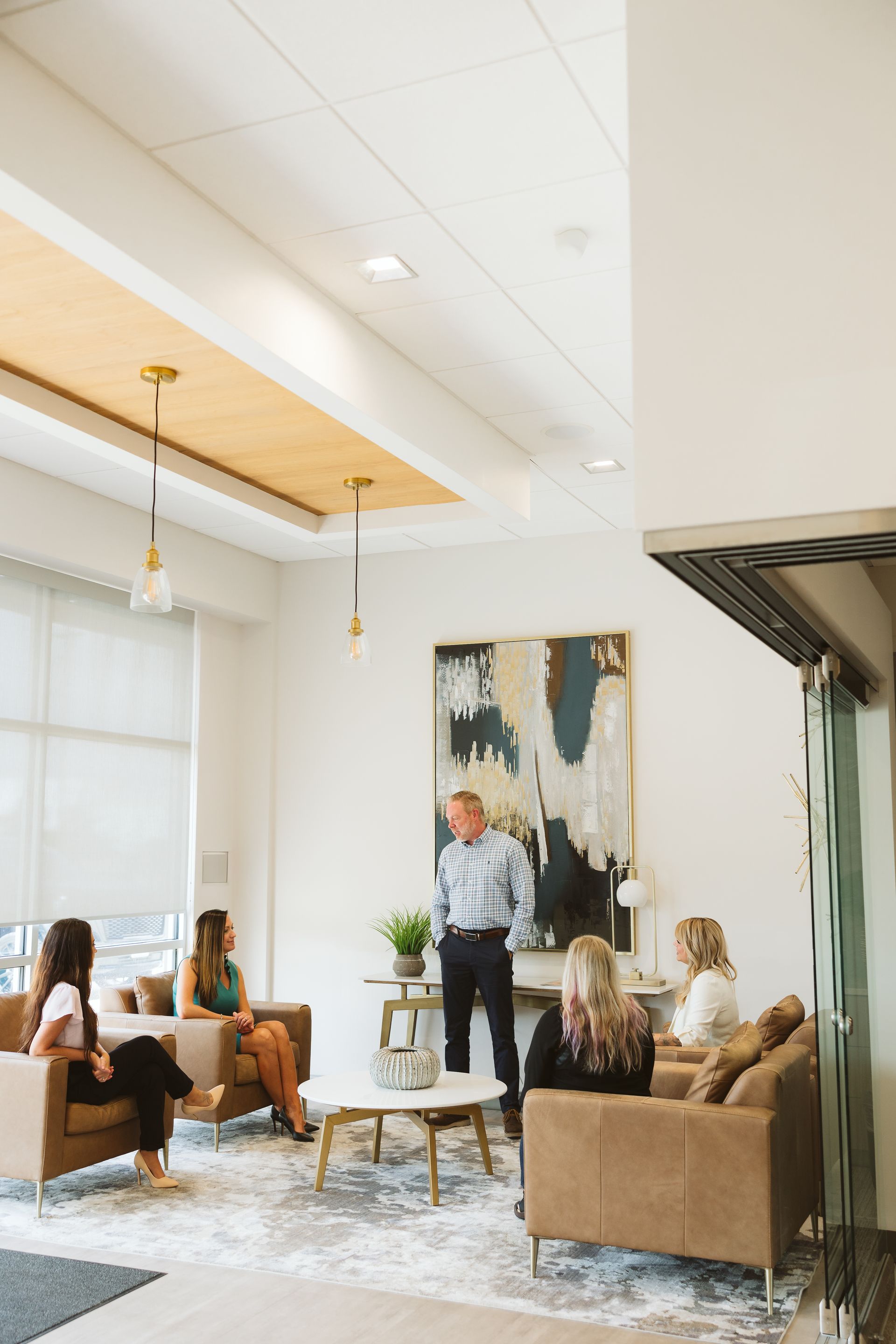 Modern office lounge with people seated and standing near a coffee table and abstract wall art