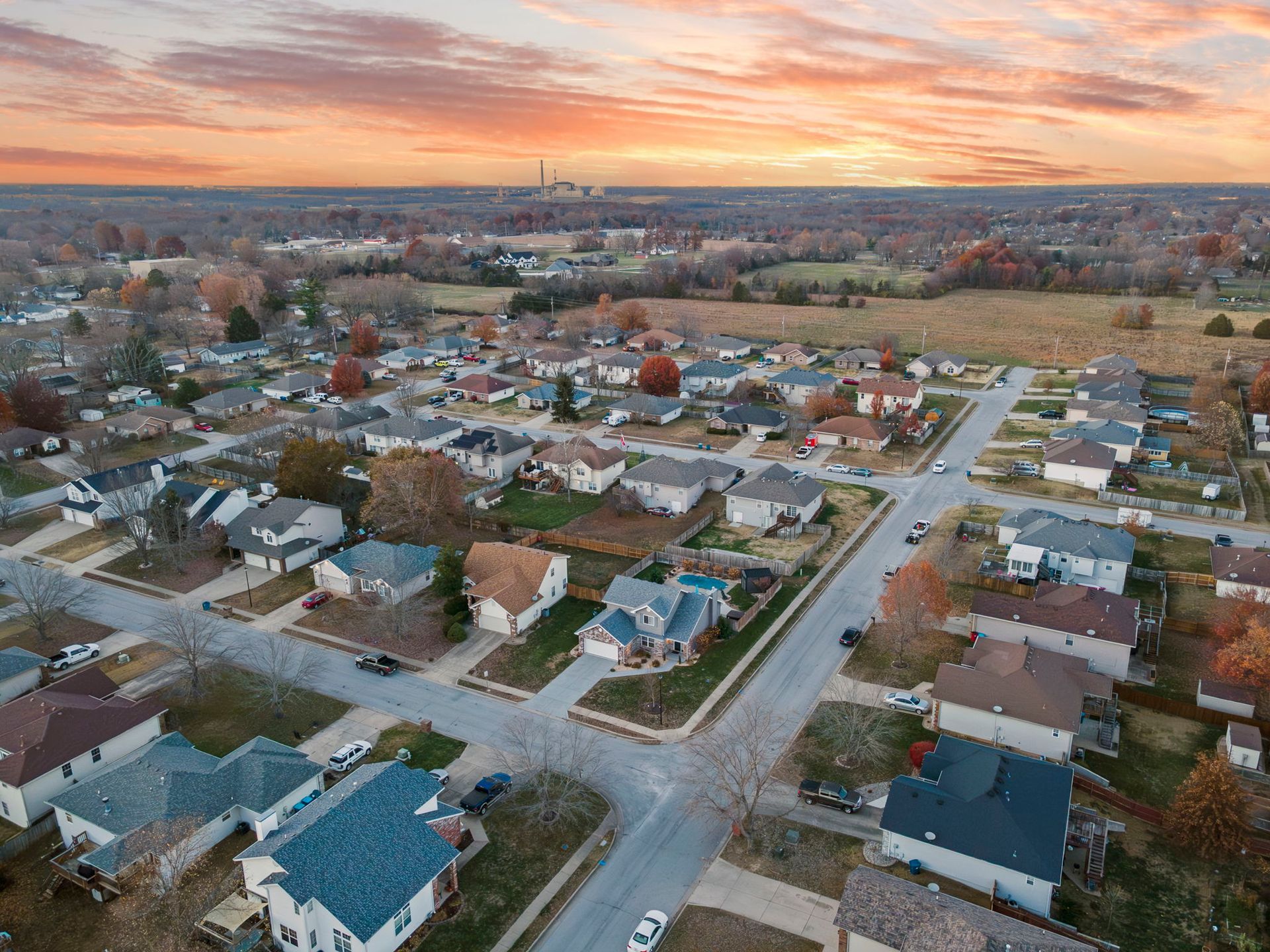 Aerial view of a suburban neighborhood with houses, streets, and autumn trees at sunset.