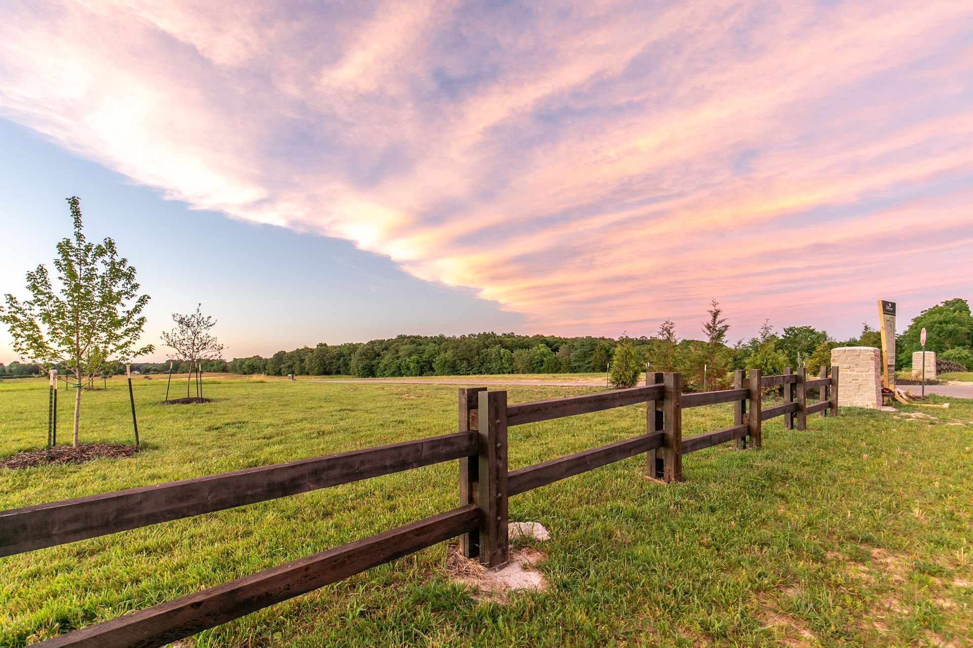 Wooden fence in a grassy field under a pink sunset sky