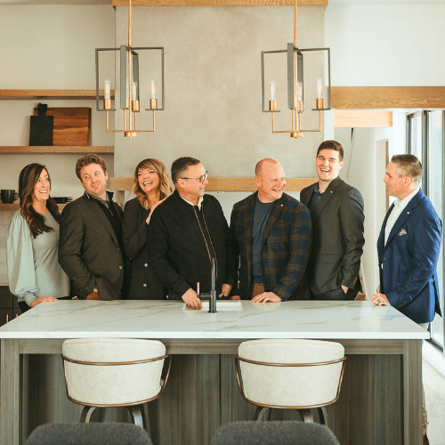 Seven people stand behind a kitchen island in a modern home, smiling during a group photo.