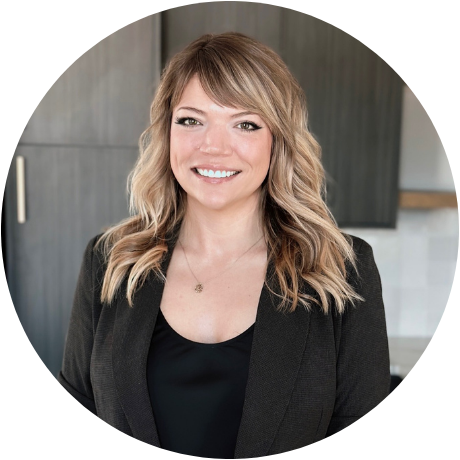 Smiling professional in black blazer, standing in a modern kitchen setting with dark cabinets.