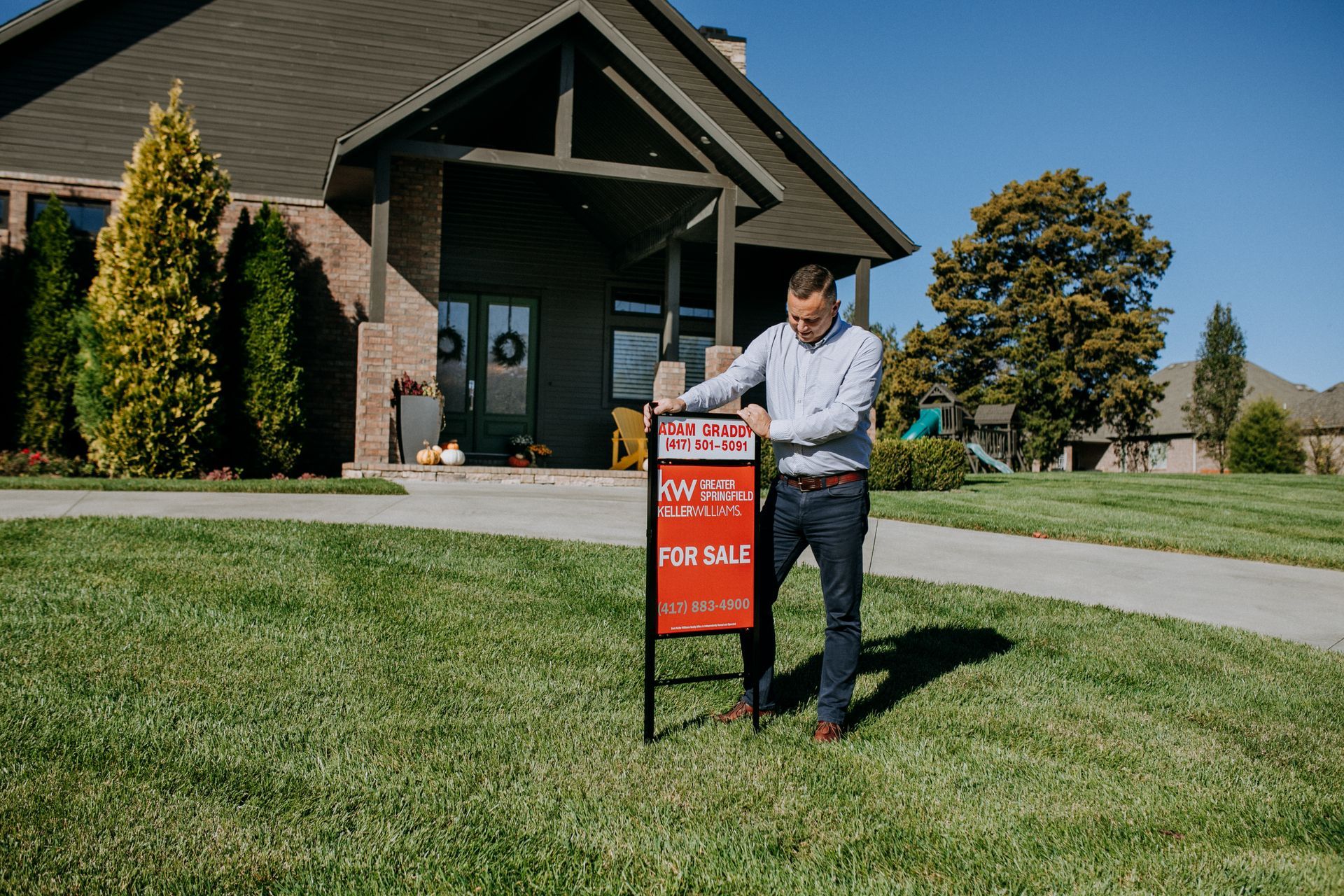 Man standing beside a red real estate sign in front of a house on a sunny lawn