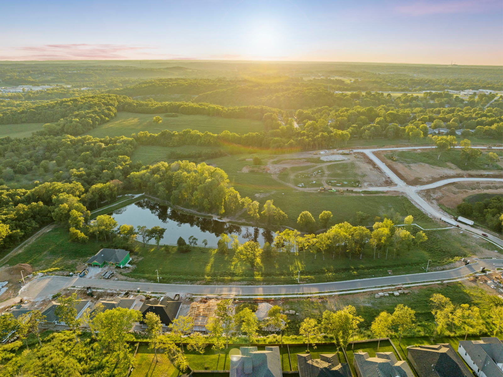 Aerial view of a green landscape with a river, road, and construction site at sunset