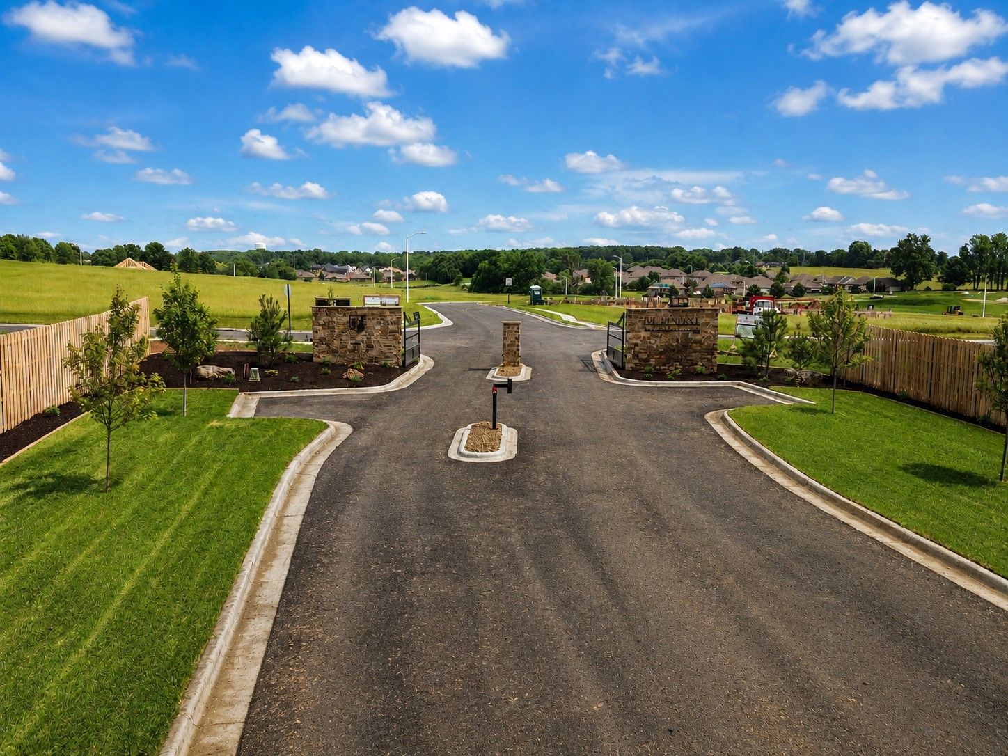New paved road leading to a gated entrance with stone pillars under a clear blue sky