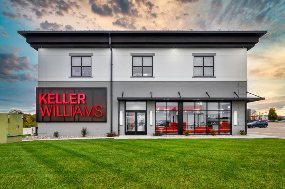 Keller Williams office building with large red signage, glass storefront, and green lawn at sunset