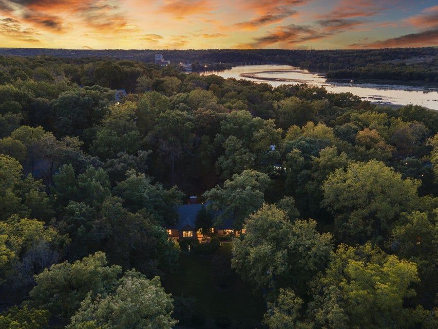 Aerial view of a forest at sunset with a river and a lit house nestled in the trees