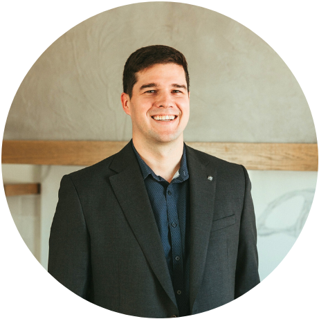 Smiling man in a dark suit standing indoors against a light wall and wooden trim