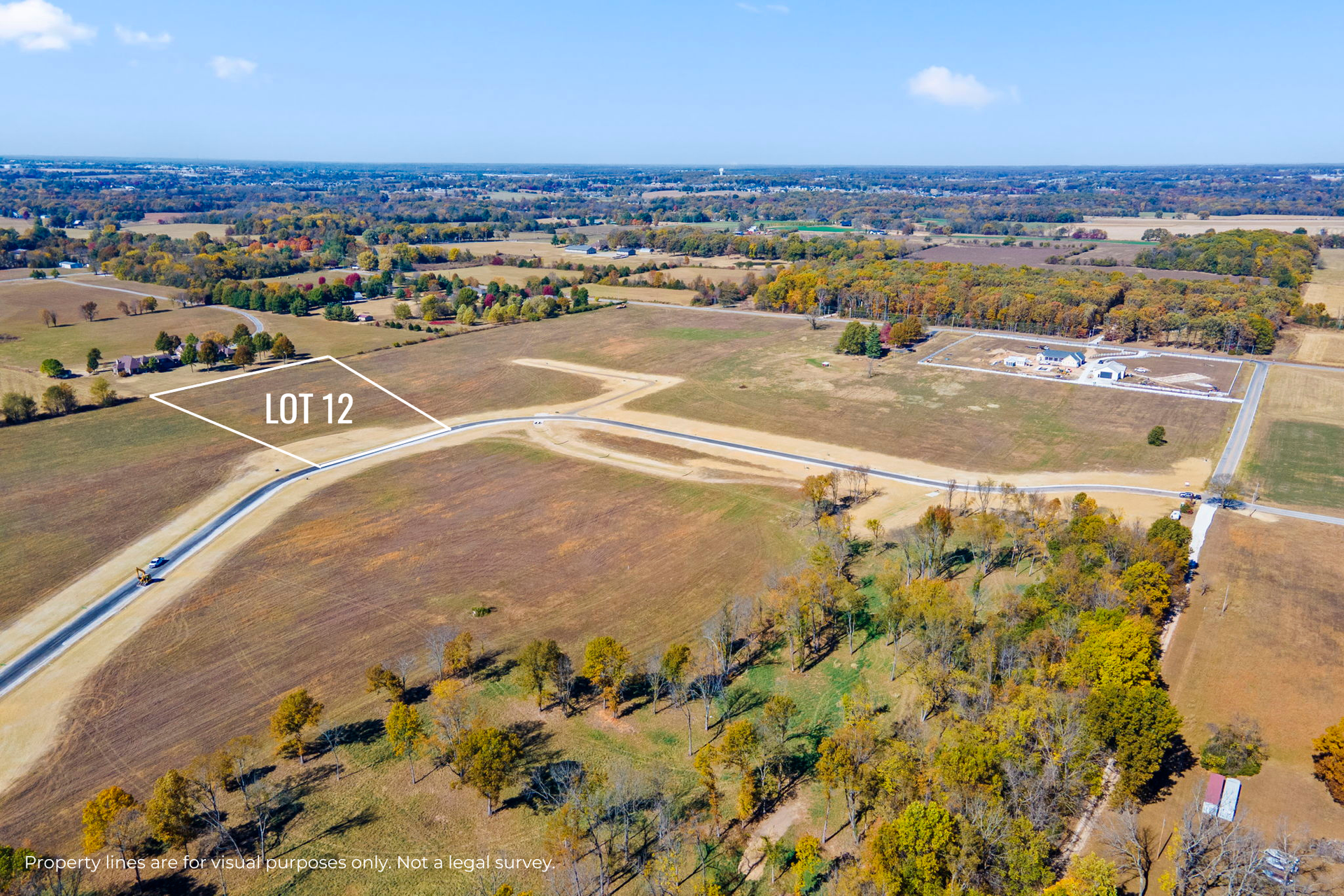 Aerial view of a rural lot with dirt roads, open fields, and distant neighborhoods under a blue sky