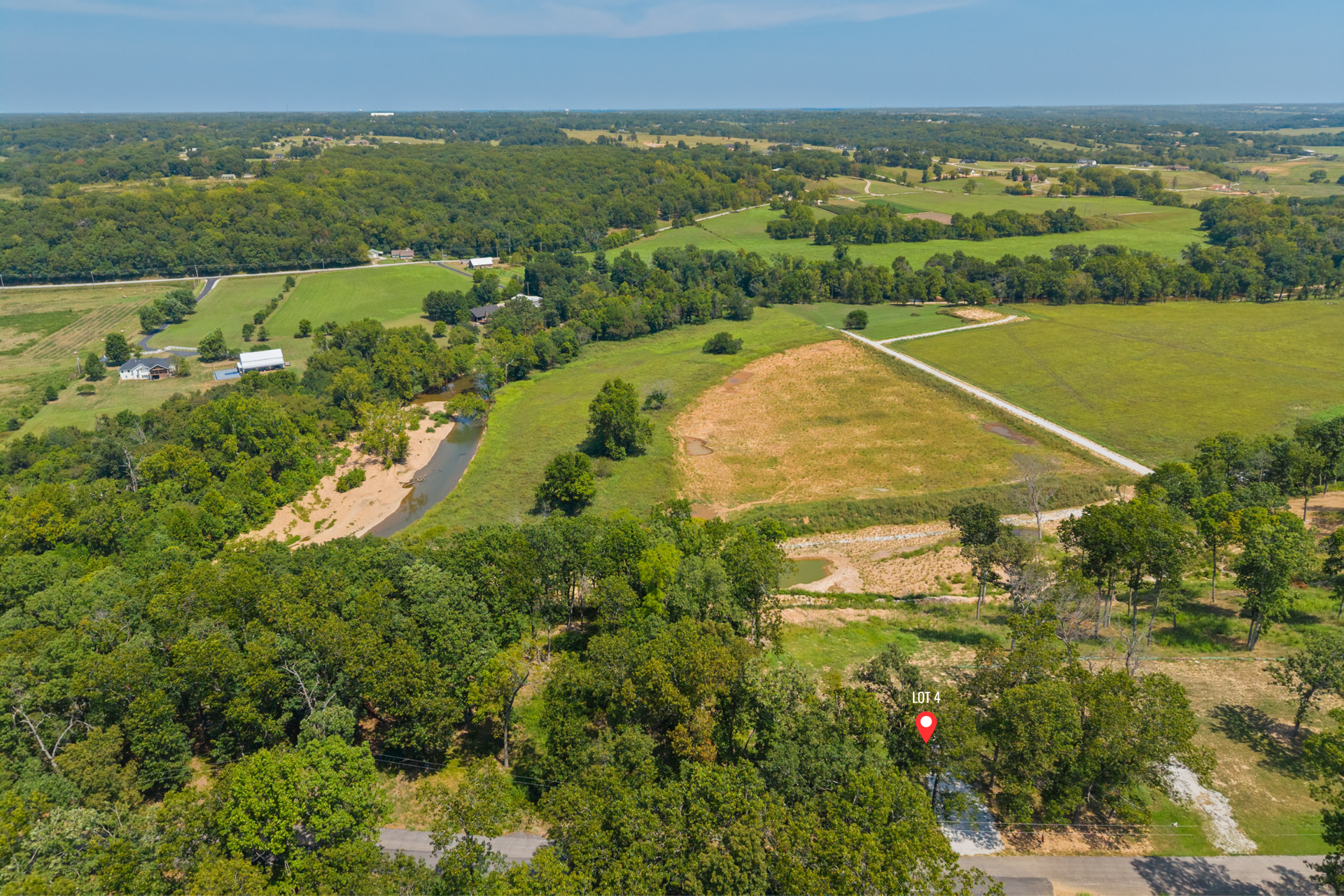 Aerial view of a wooded landscape with a fenced clearing and winding road.