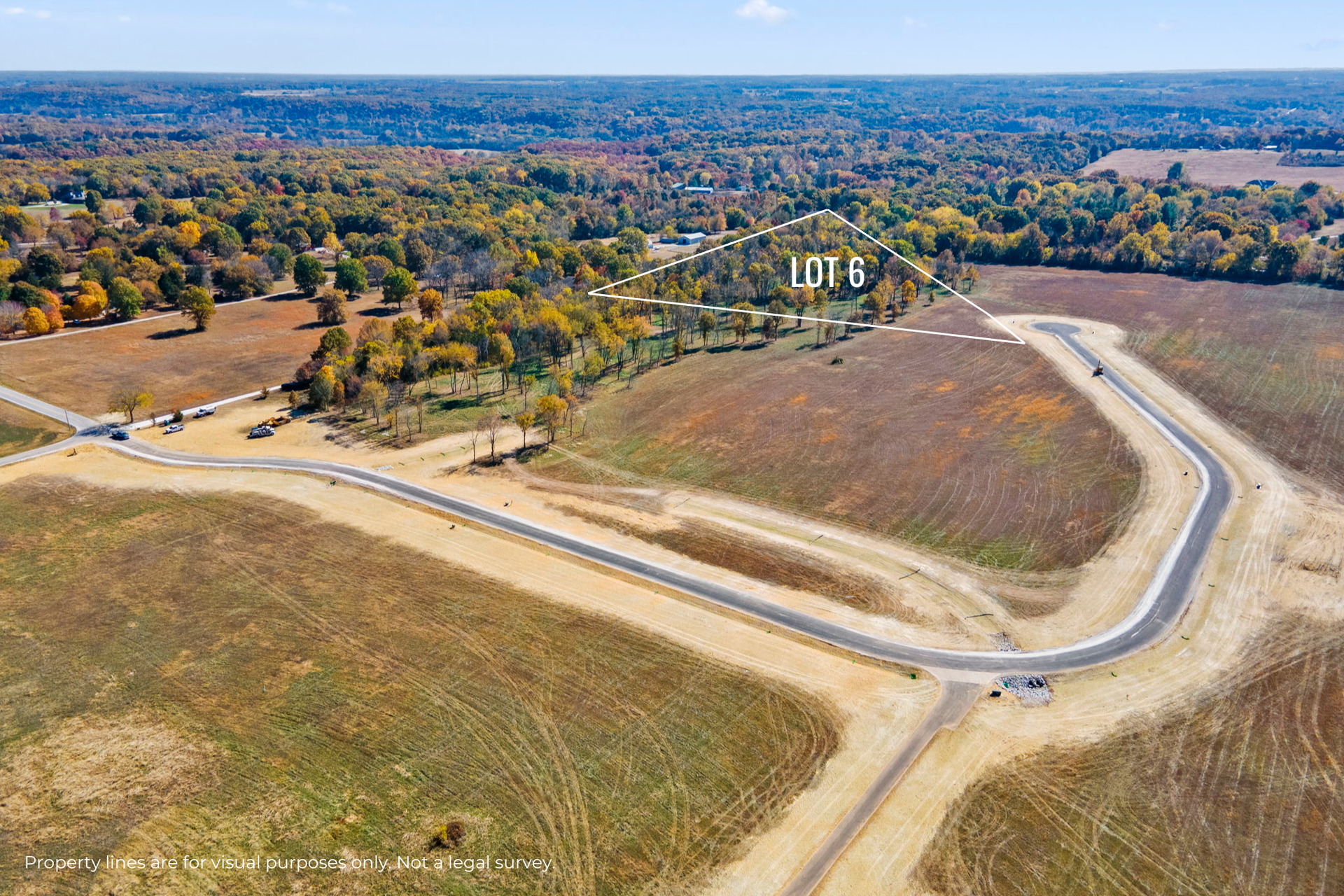 Aerial view of a curving dirt road through open grassy fields with trees in the distance