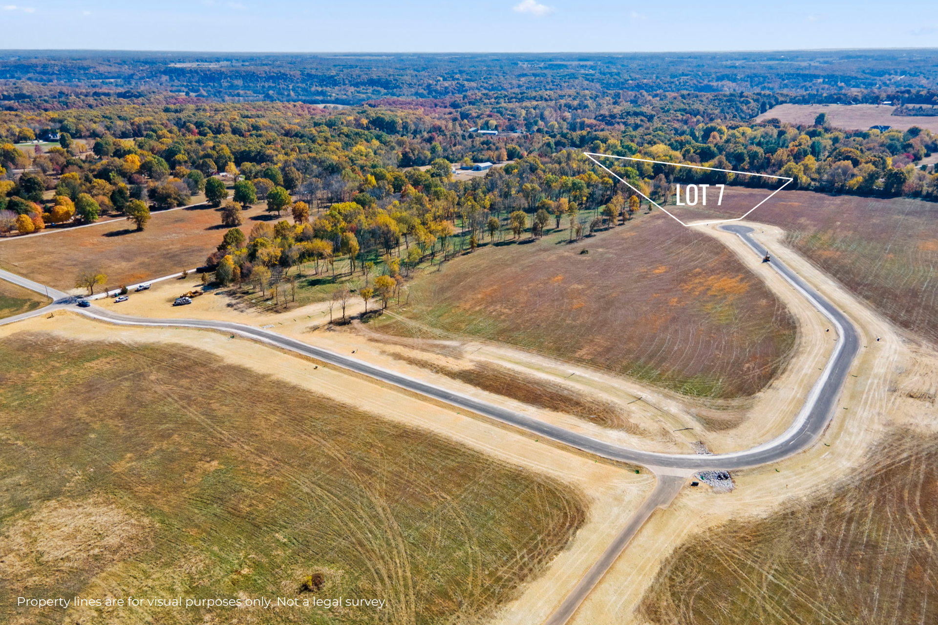Aerial view of a winding road through brown fields and autumn trees under a blue sky