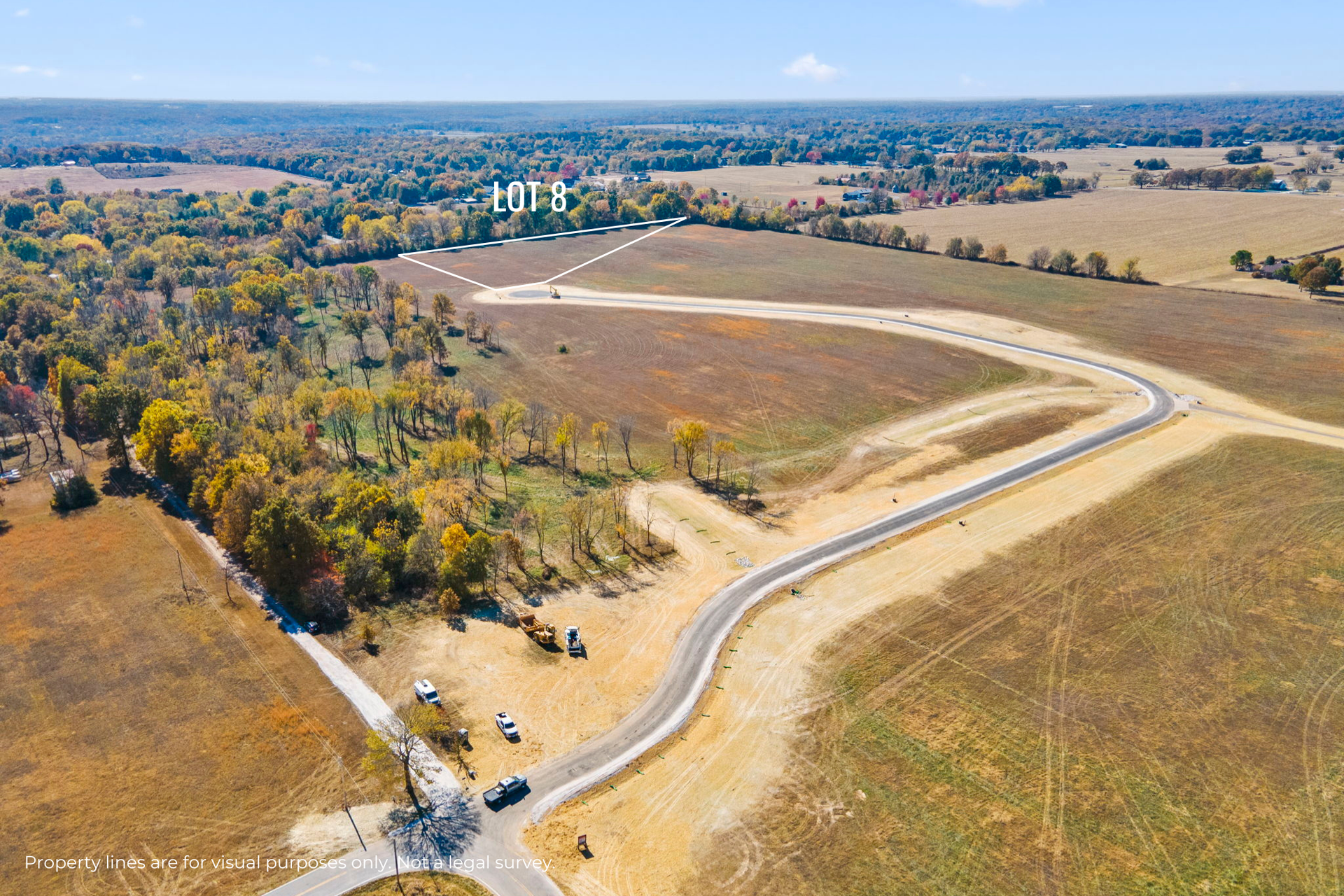 Aerial view of a winding rural road beside open fields and autumn trees near a distant building