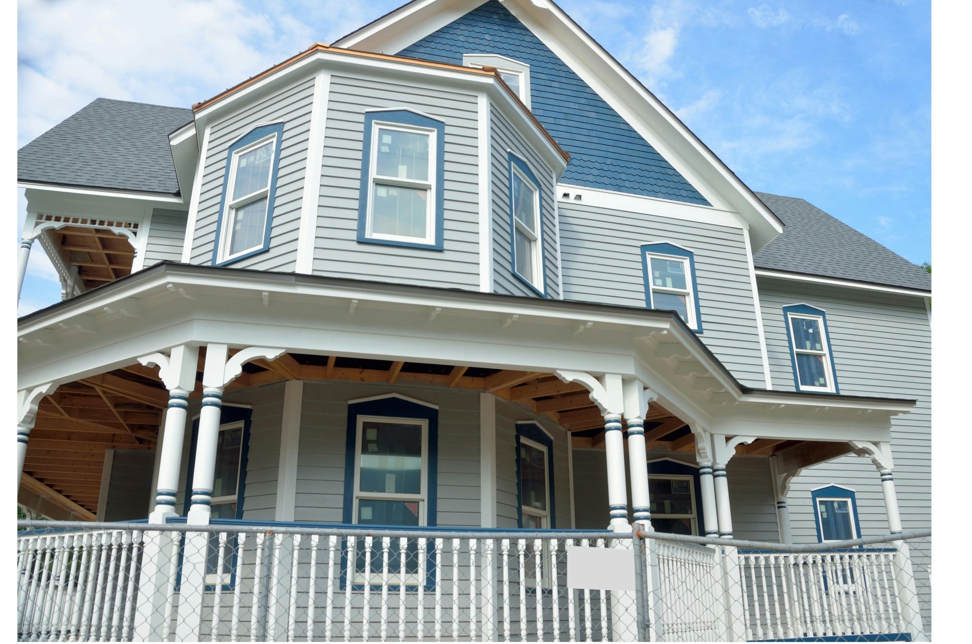 Gray two-story house with white trim, bay windows, and a covered front porch under a blue sky