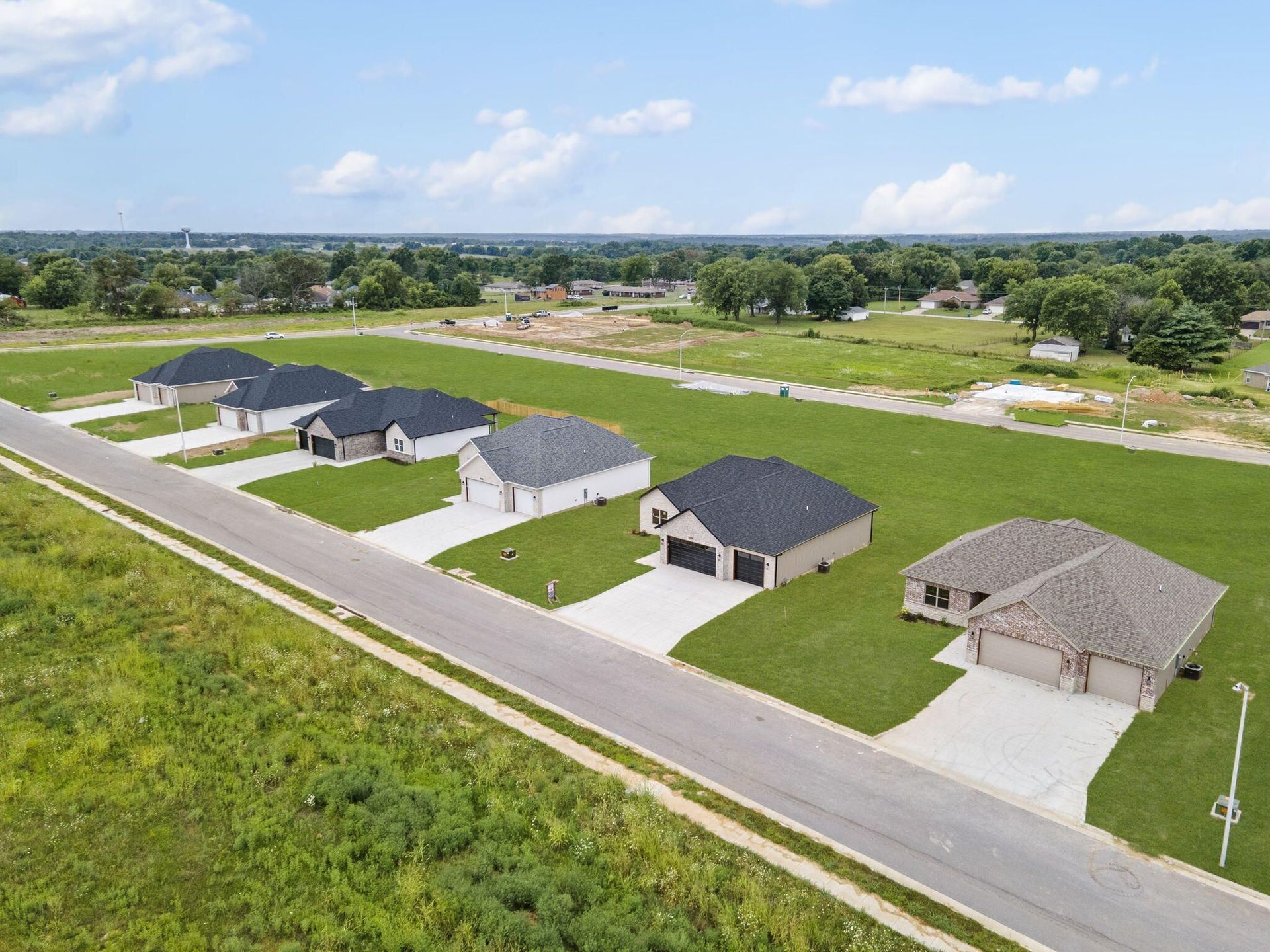 Aerial view of modern homes along a road beside green fields under a clear blue sky