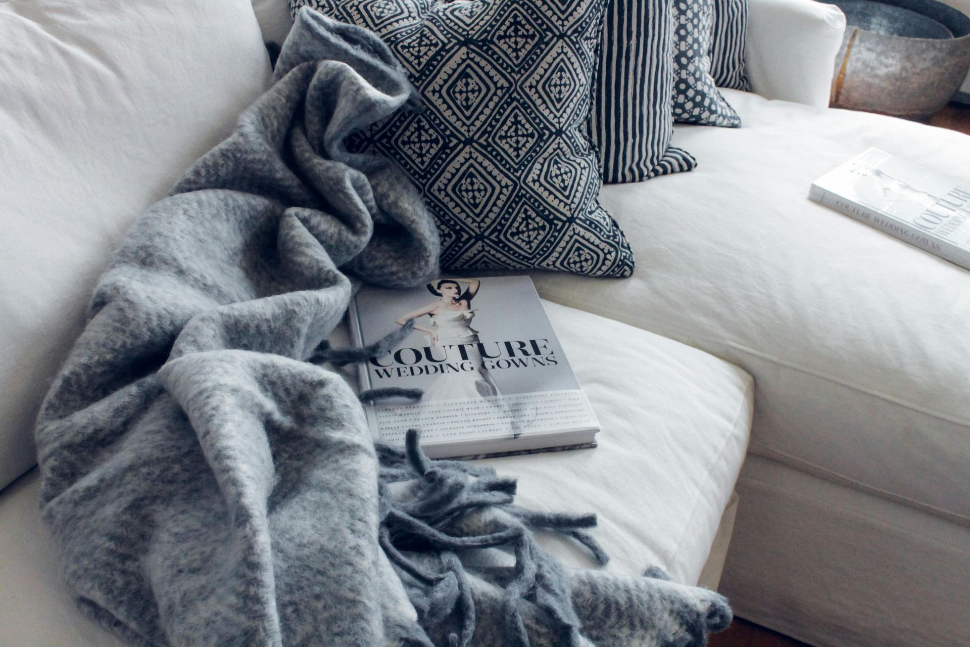 Cozy white sofa with gray knit throw, patterned pillows, and a magazine on the seat