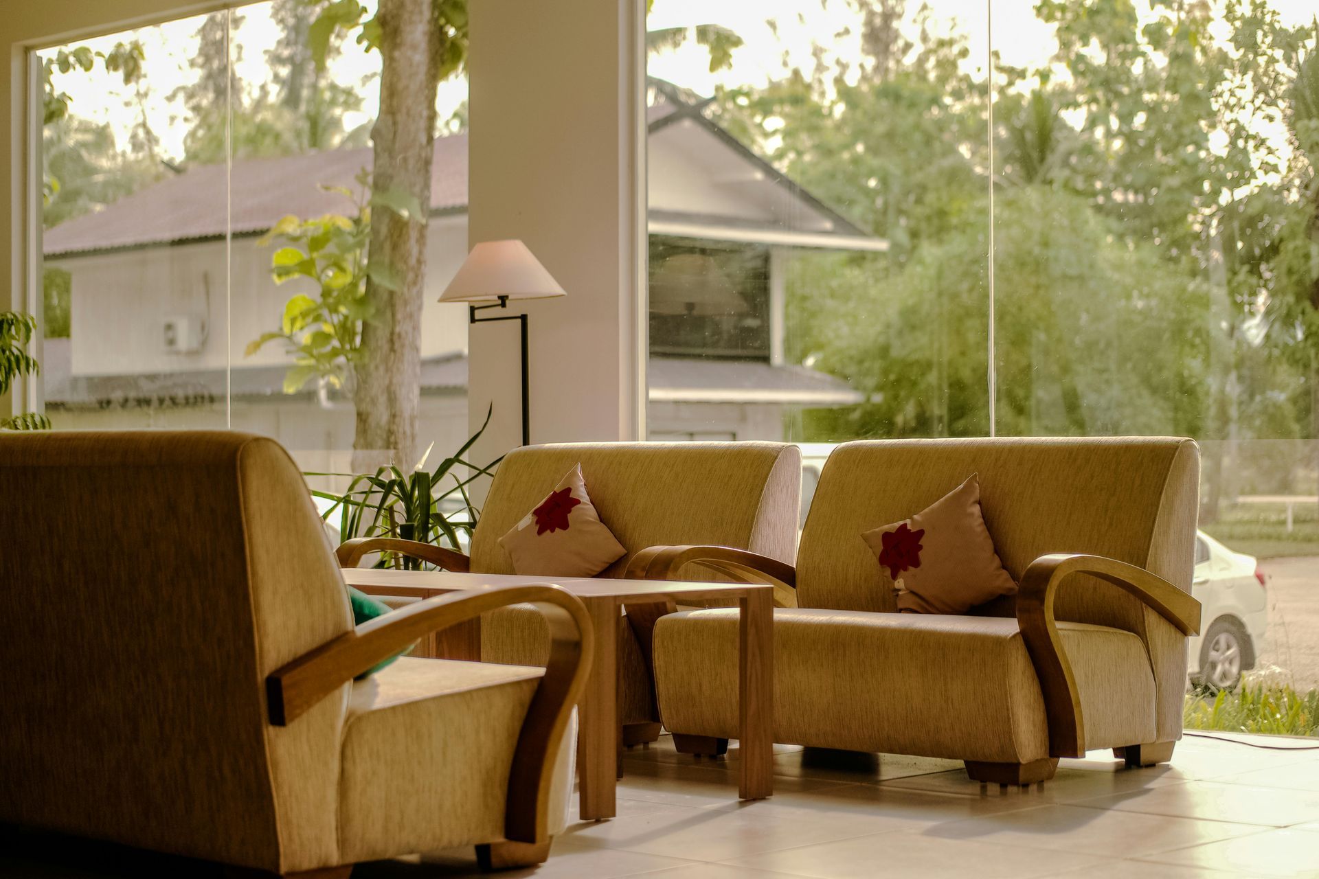 Modern living room with wicker chairs, tan cushions, and large windows overlooking trees and a house