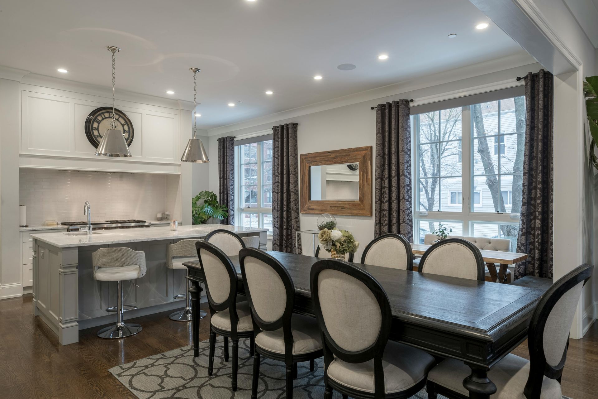 Bright modern dining room with oval table, upholstered chairs, kitchen island, and large windows