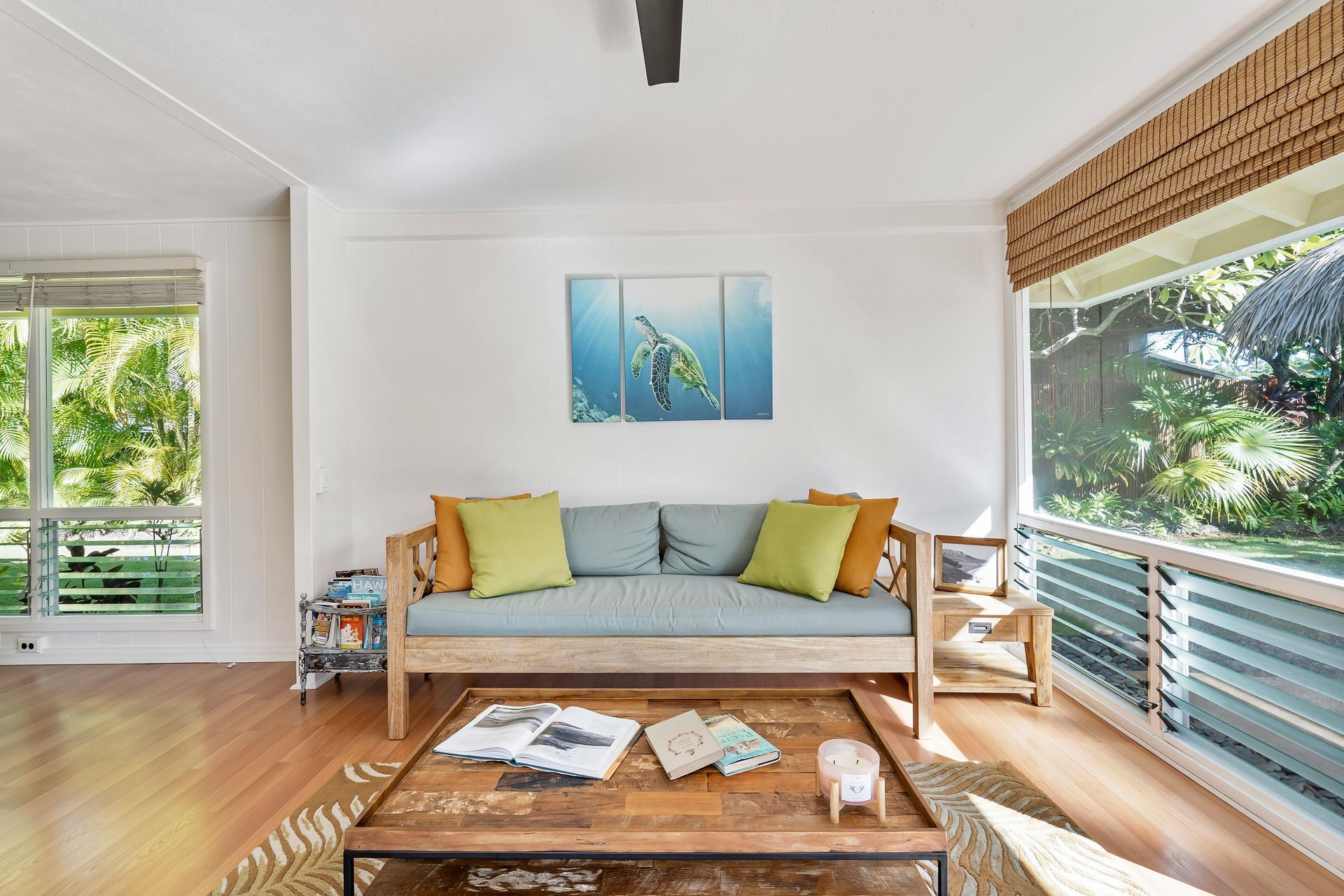 Bright living room with sofa, coffee table, wood floors, and large windows overlooking greenery