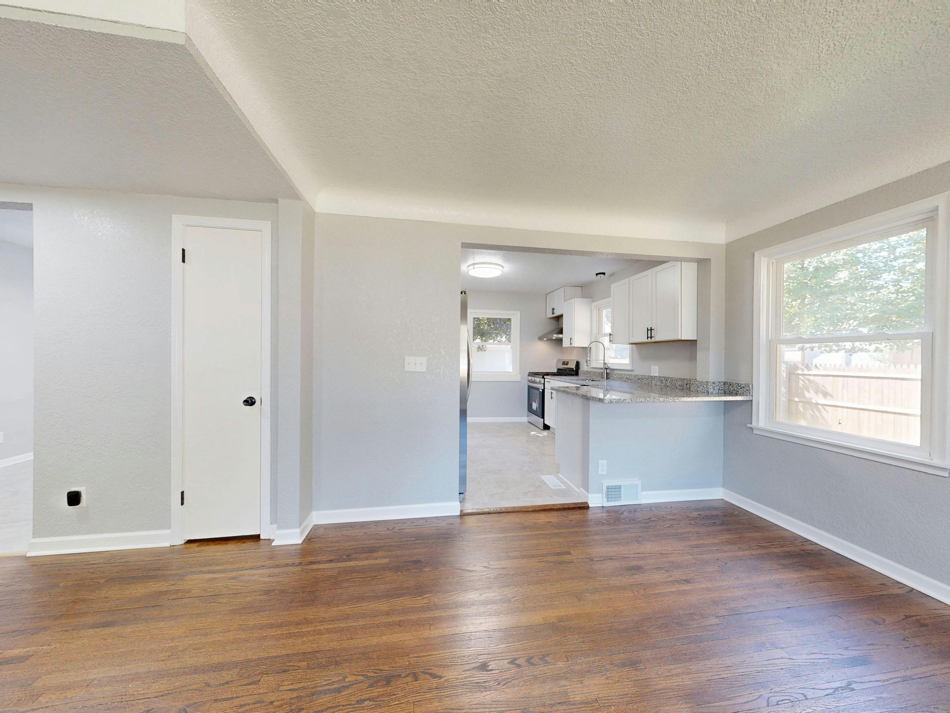 Empty living room with hardwood floors, gray walls, and a kitchen pass-through in the background