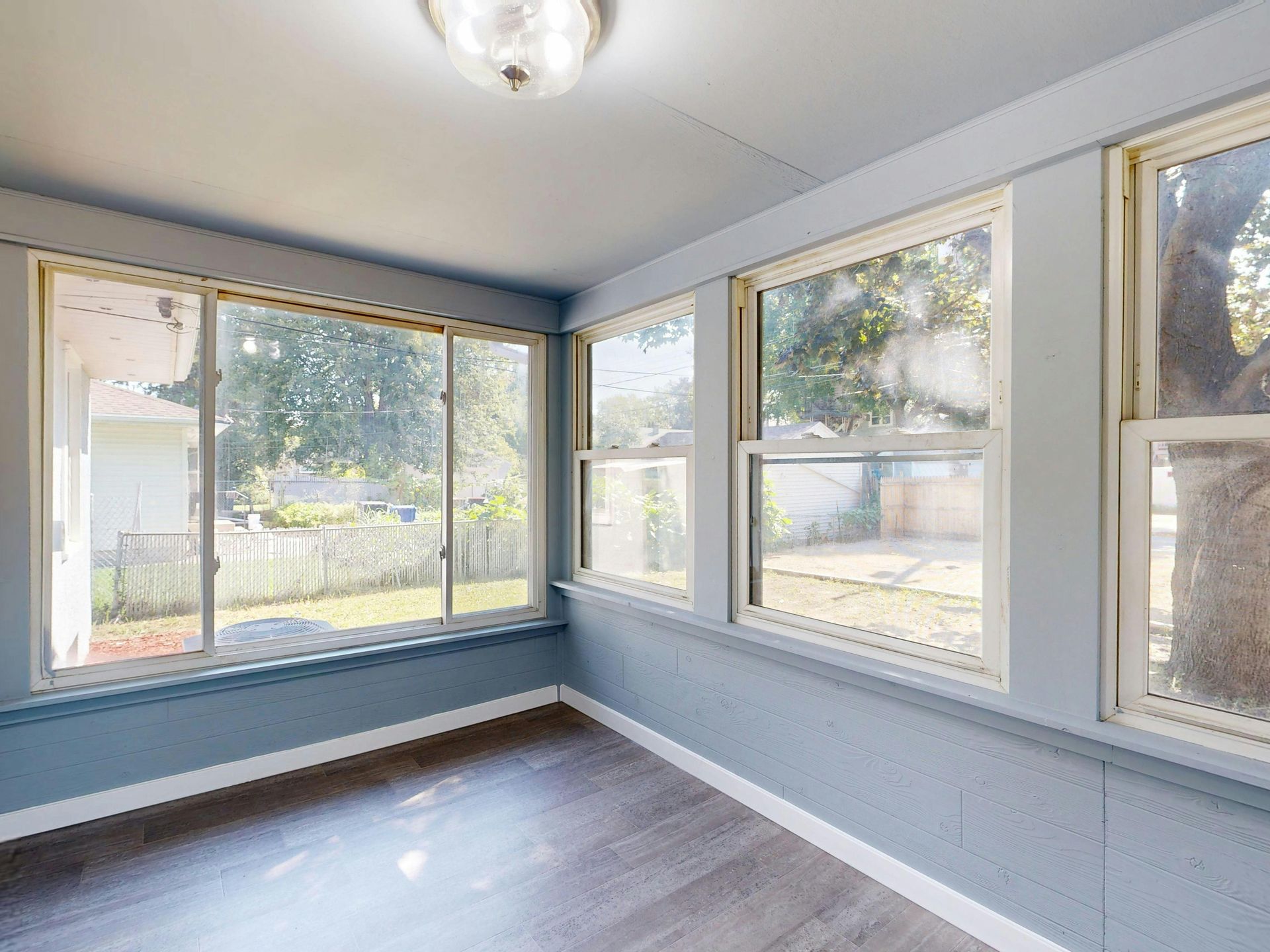 Bright empty sunroom with large windows, light blue walls, and dark wood floors.