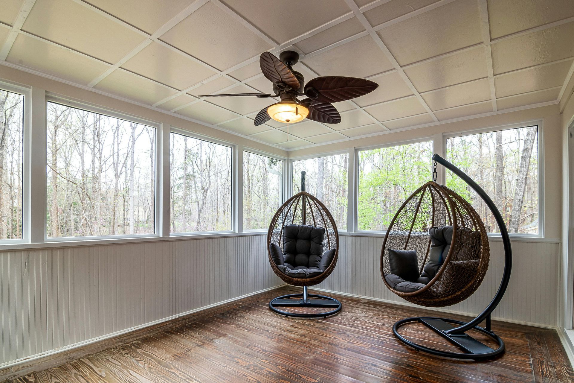 Sunroom with two hanging egg chairs, wood floor, screened windows, and ceiling fan