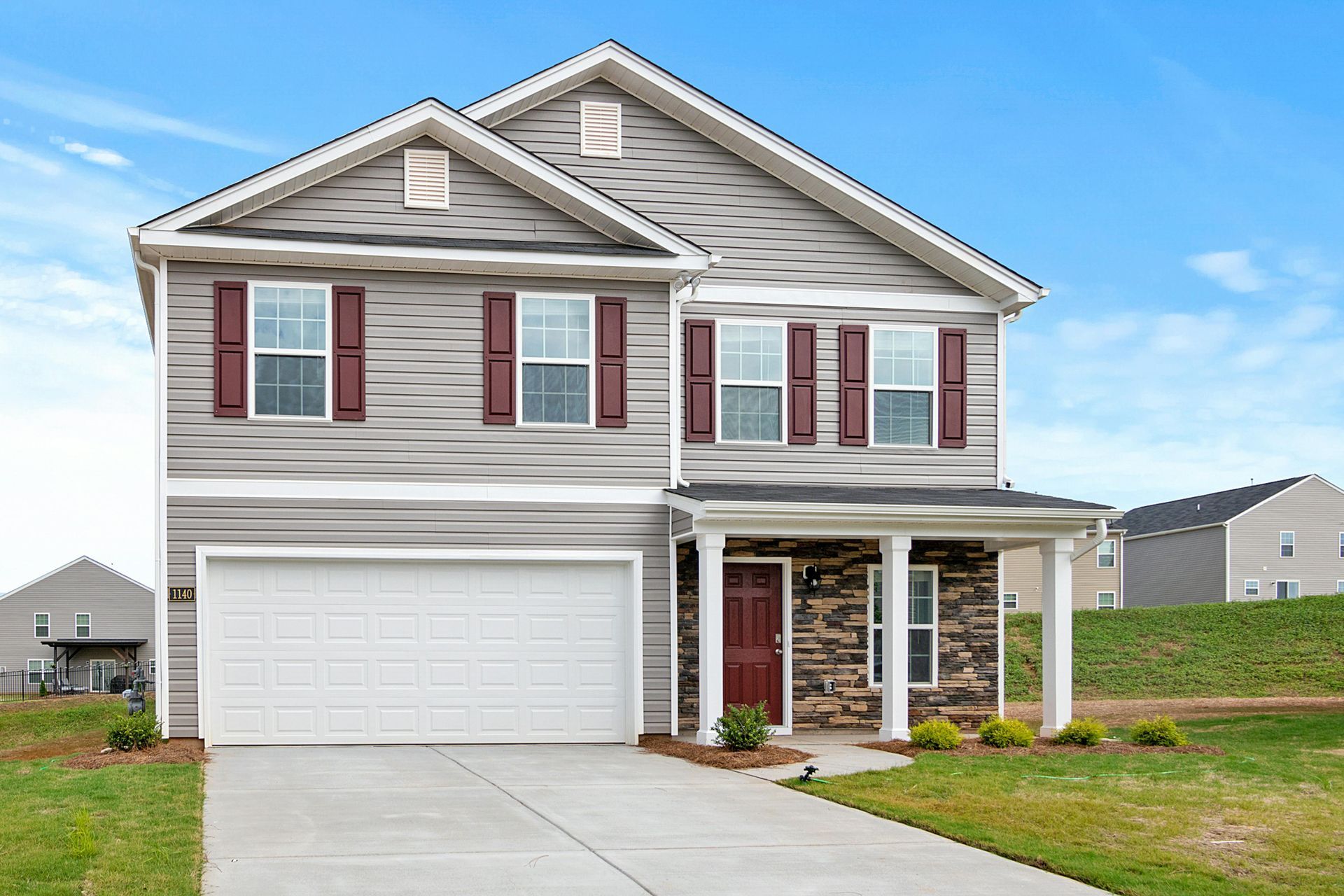 Two-story gray house with white trim, red shutters, and a two-car garage on a suburban street.