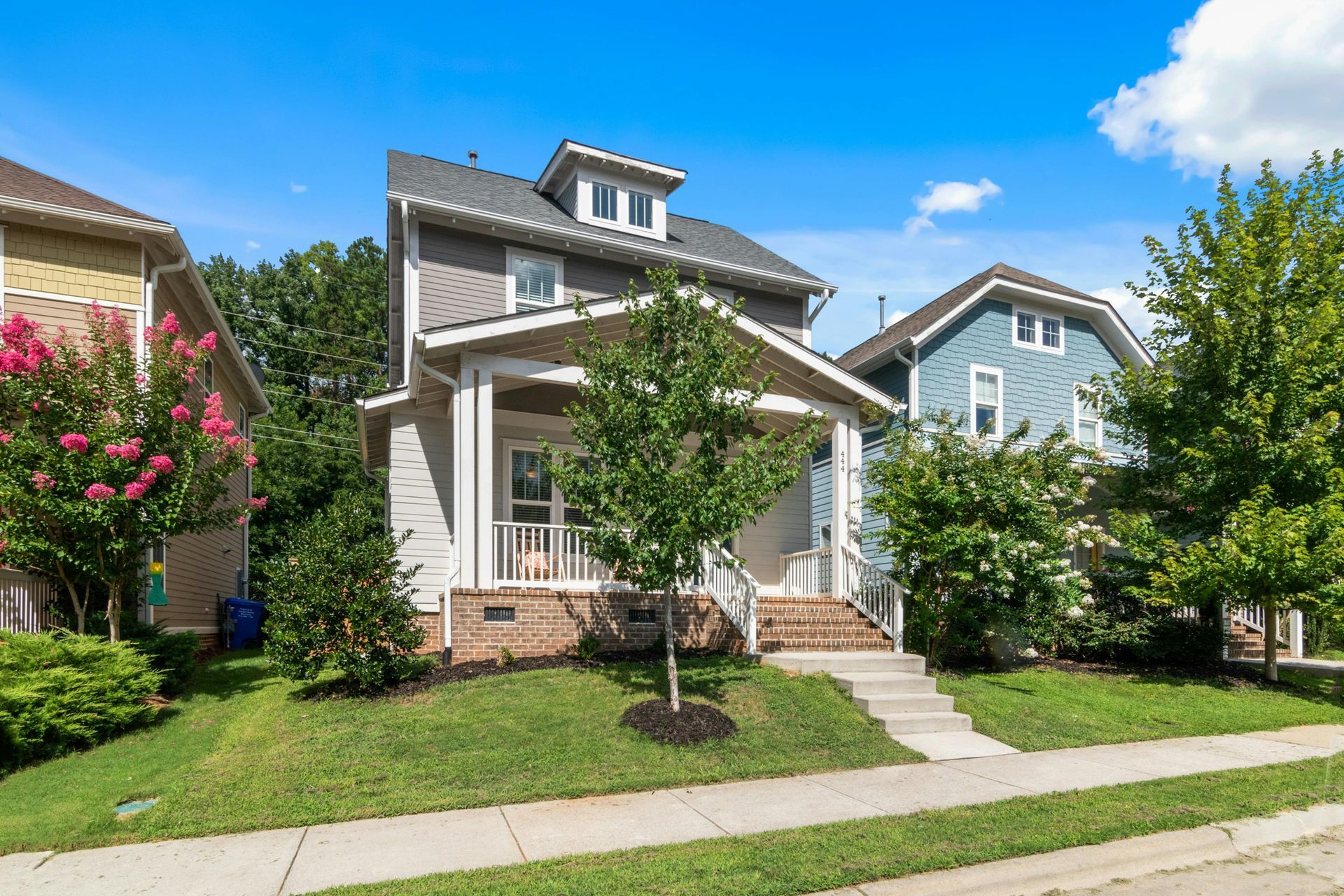 Two-story suburban house with white trim, front porch, and landscaped yard on a sunny day