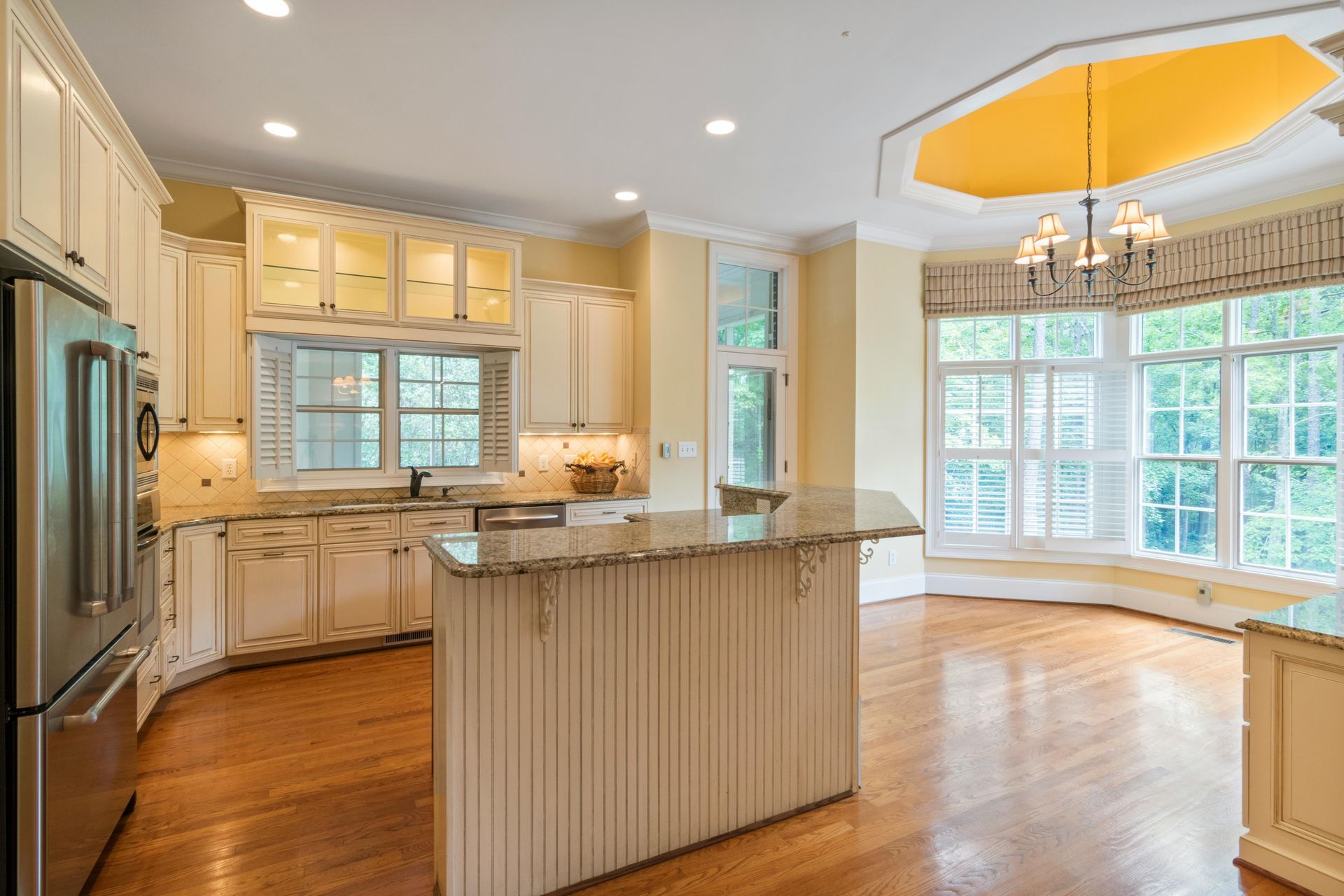 Bright kitchen with white cabinets, island, hardwood floors, and large sunlit windows into dining area