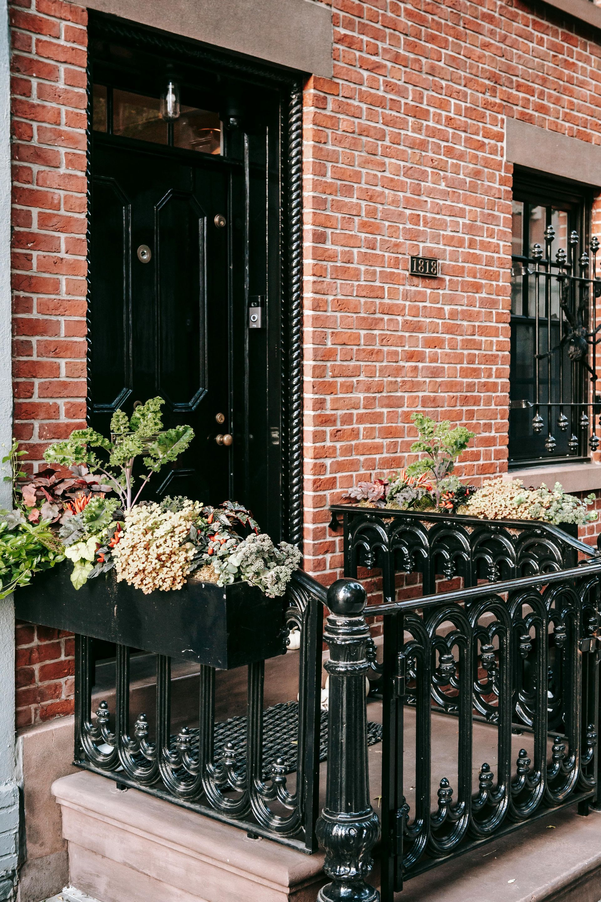 Brick townhouse entrance with black iron gate and flower boxes on a narrow stoop