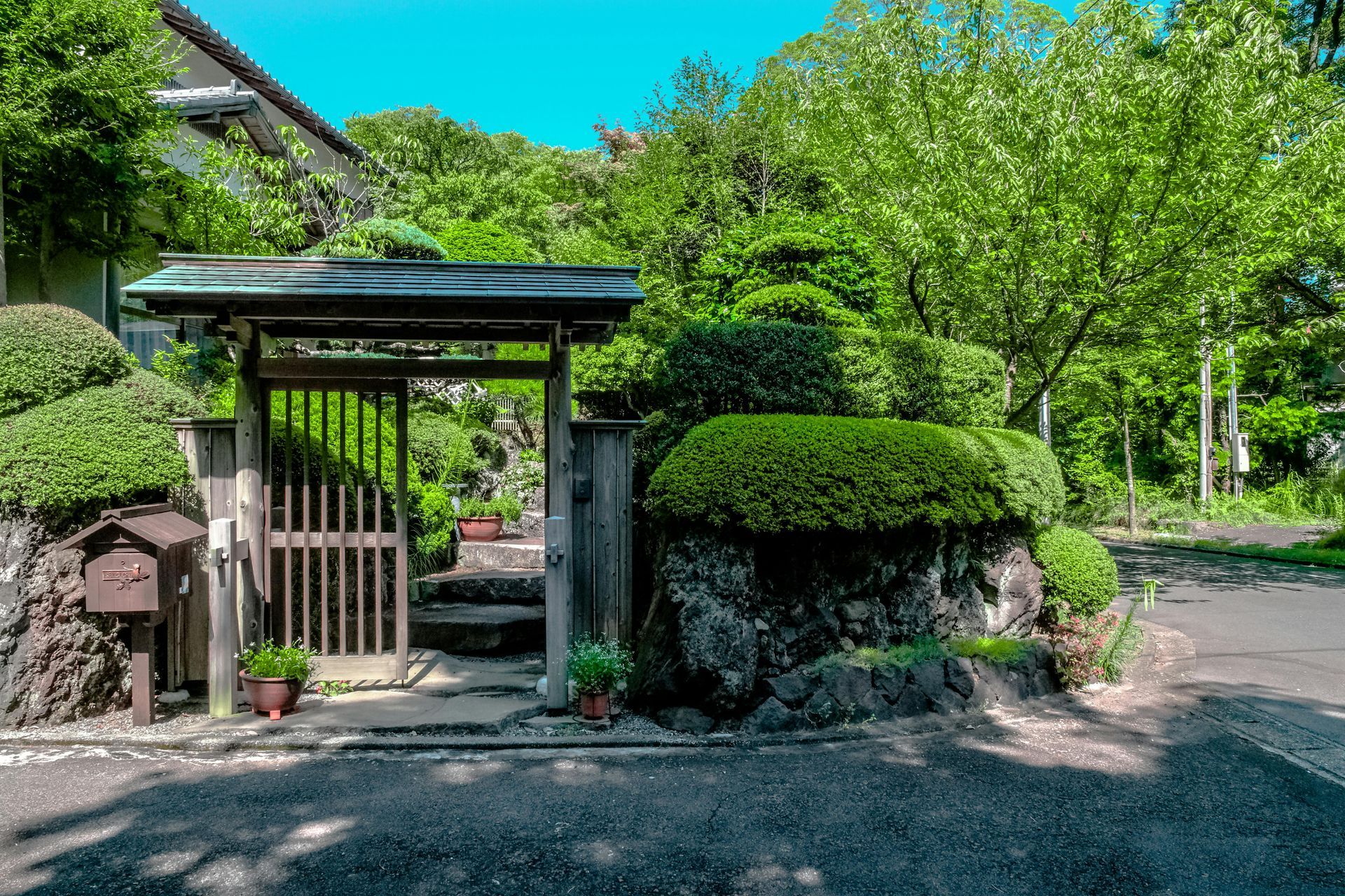 Traditional Japanese garden entrance with wooden gate, stone wall, and lush green trees