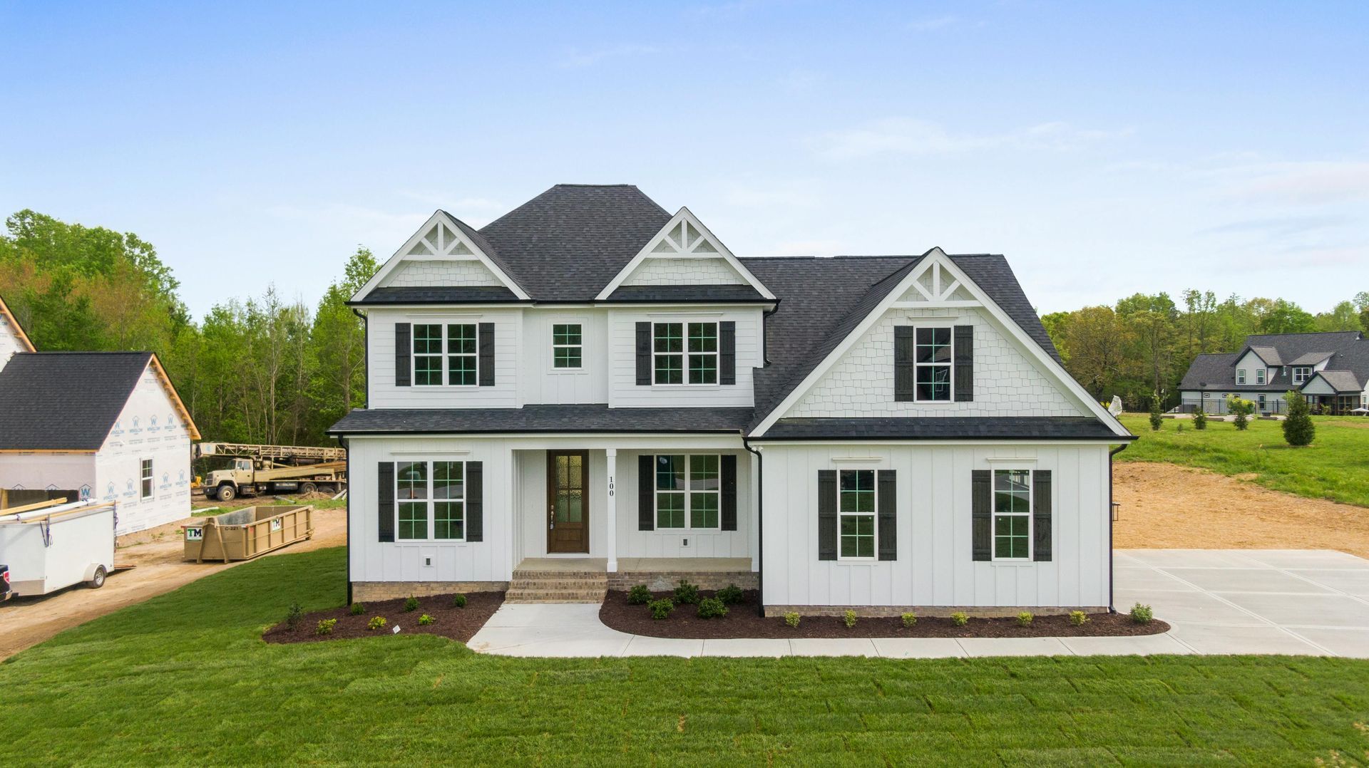 New white two-story house with dark roof and green shutters on a landscaped lot