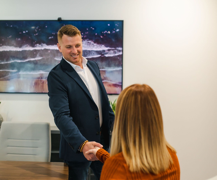 Man in a dark suit shaking hands across a conference table in a modern office
