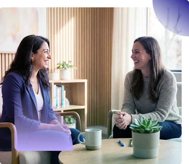 Two coworkers smiling while looking at a laptop at a table near a window