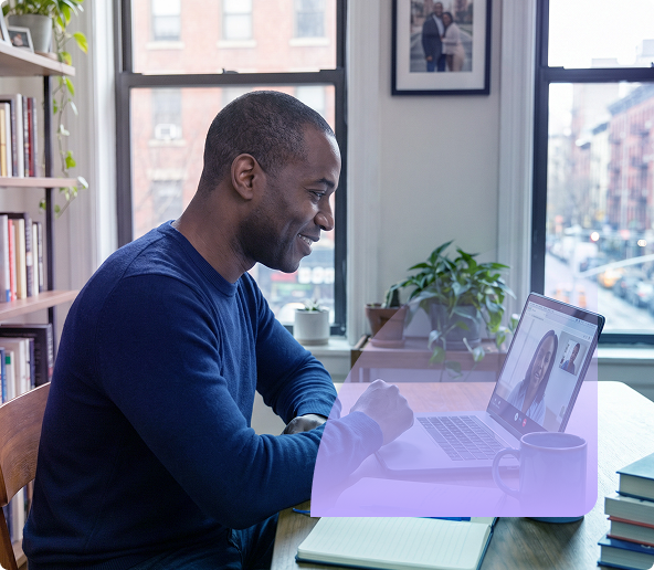 Man smiling while typing on a laptop at a desk with a coffee mug in a bright home office