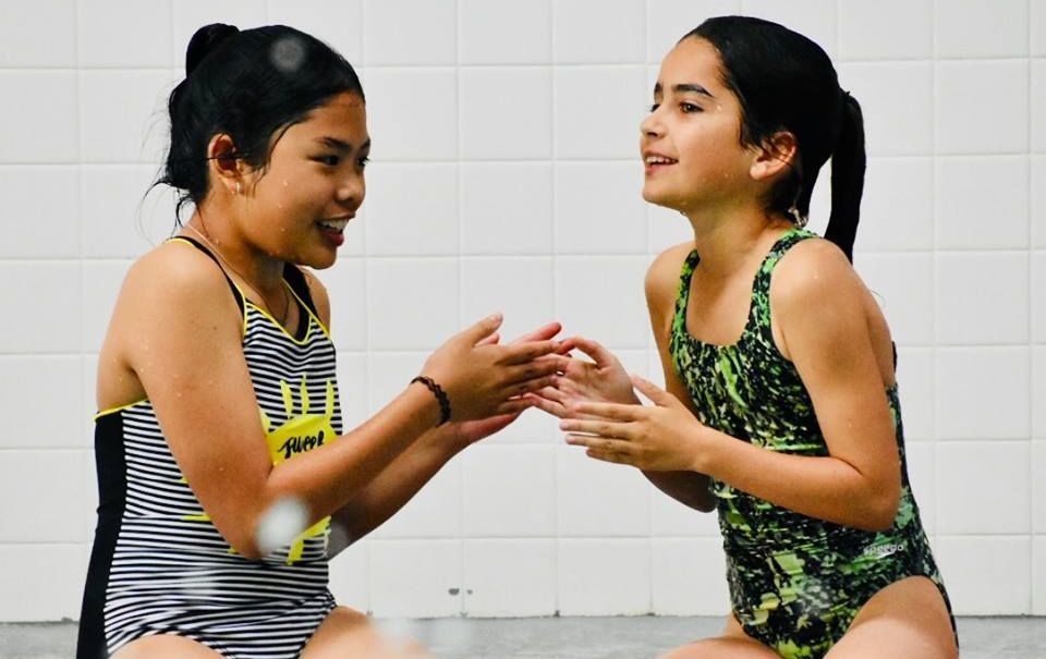 Two young girls in swimsuits are sitting next to each other and shaking hands.