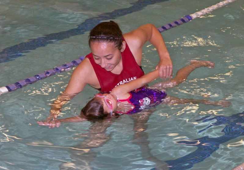 A woman is teaching a little girl how to swim in a pool.