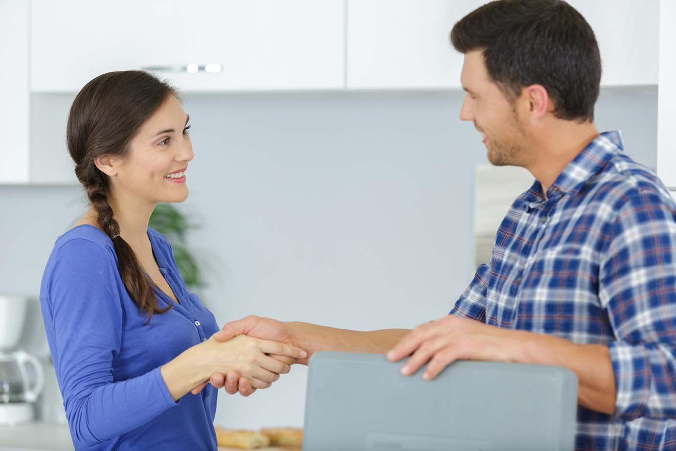 A man and a woman are shaking hands in a kitchen.