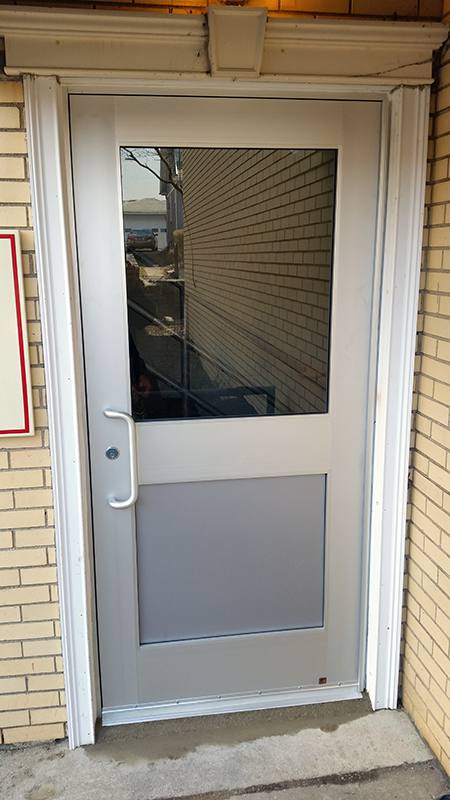 A white door with a glass window is on a brick building.