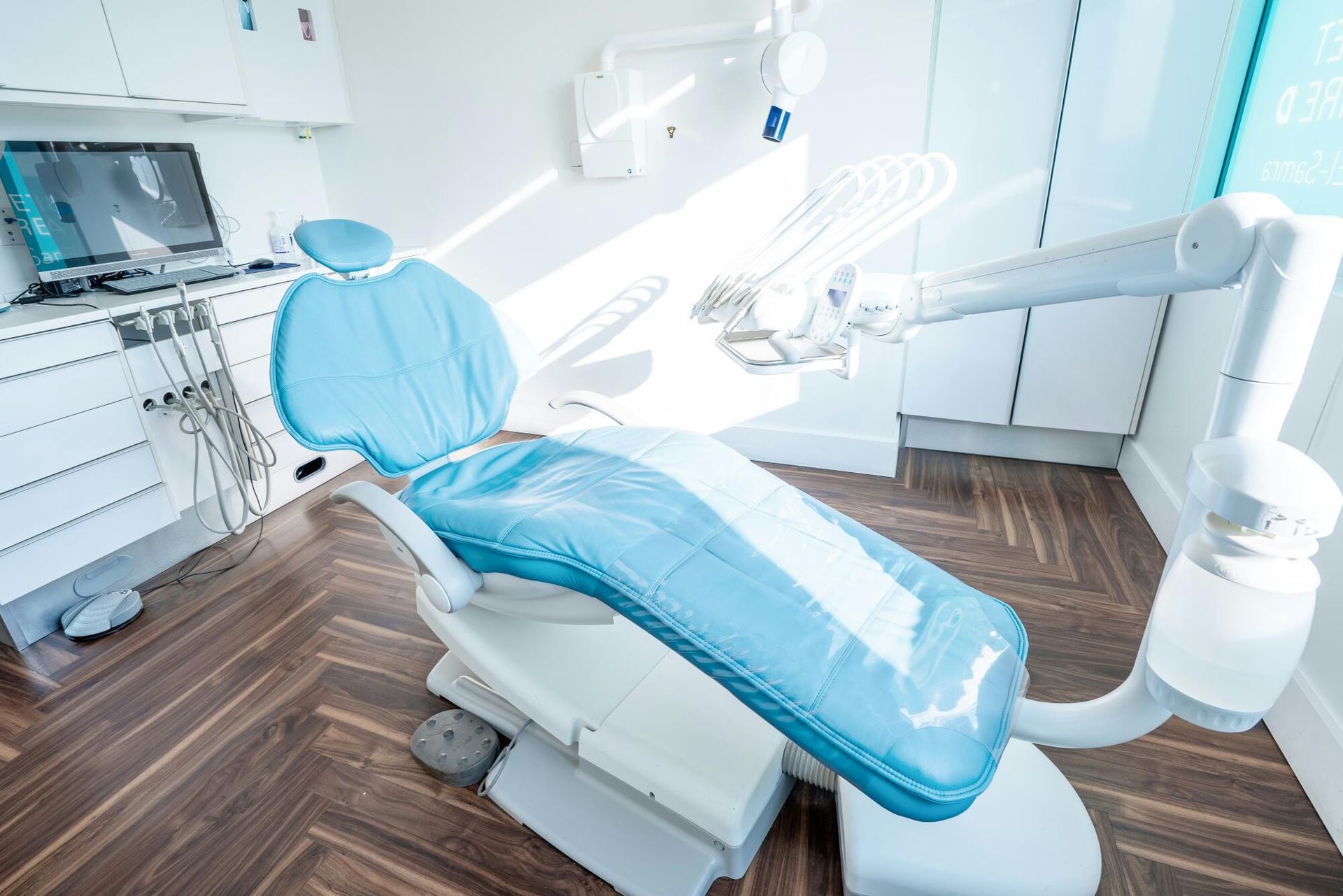 Modern dental exam room with blue chair, overhead lamp, and white equipment arms