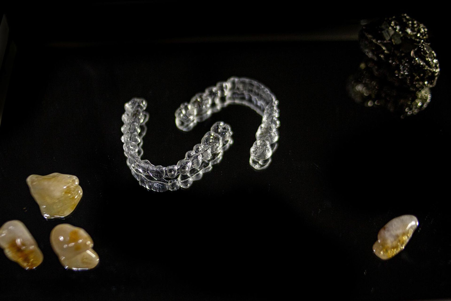 Clear aligners arranged with rock fragments on a black surface.
