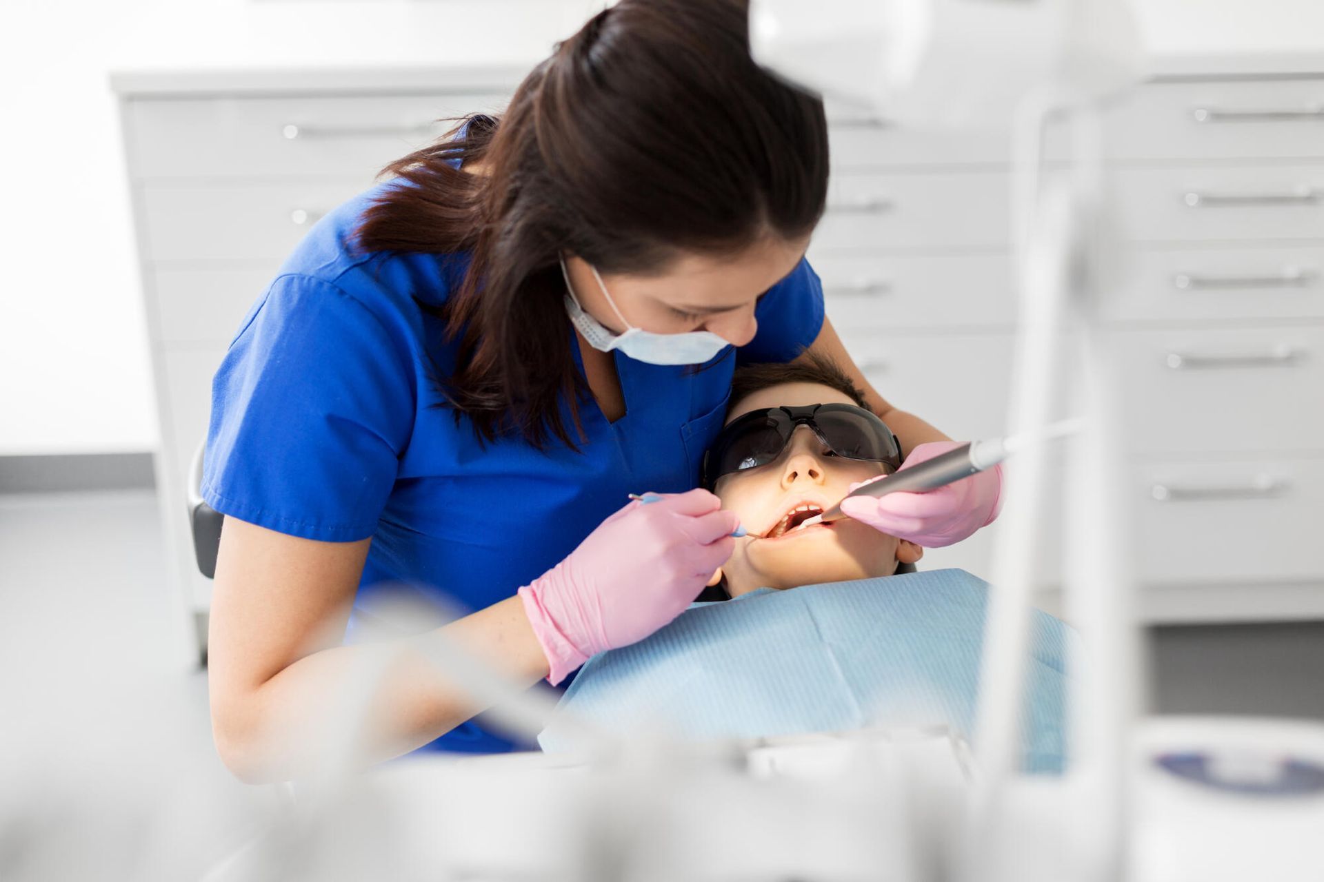 Dentist in blue scrubs examining a patient’s teeth in a bright clinic