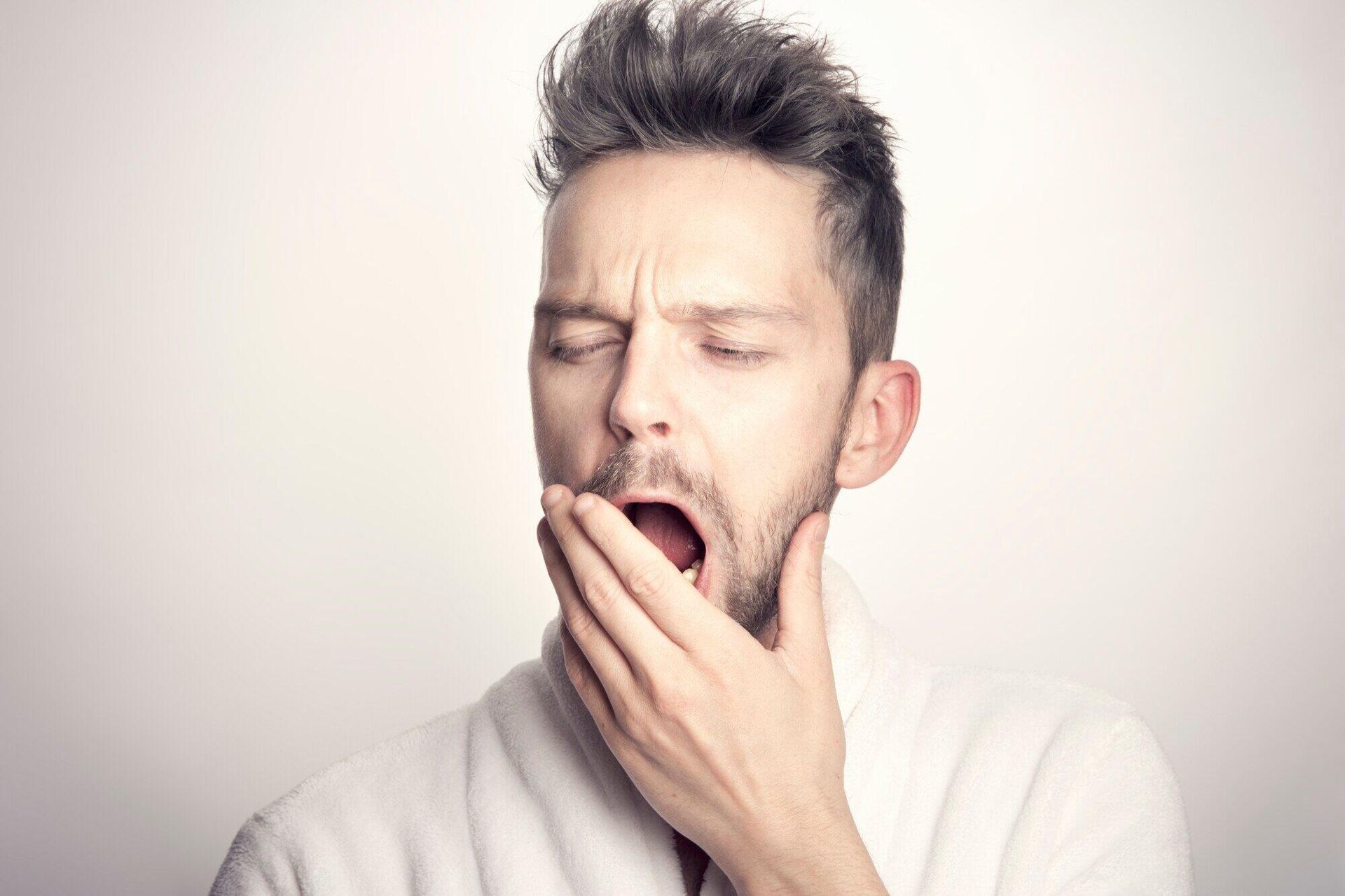 Man yawning and covering his mouth with his hand against a plain light background