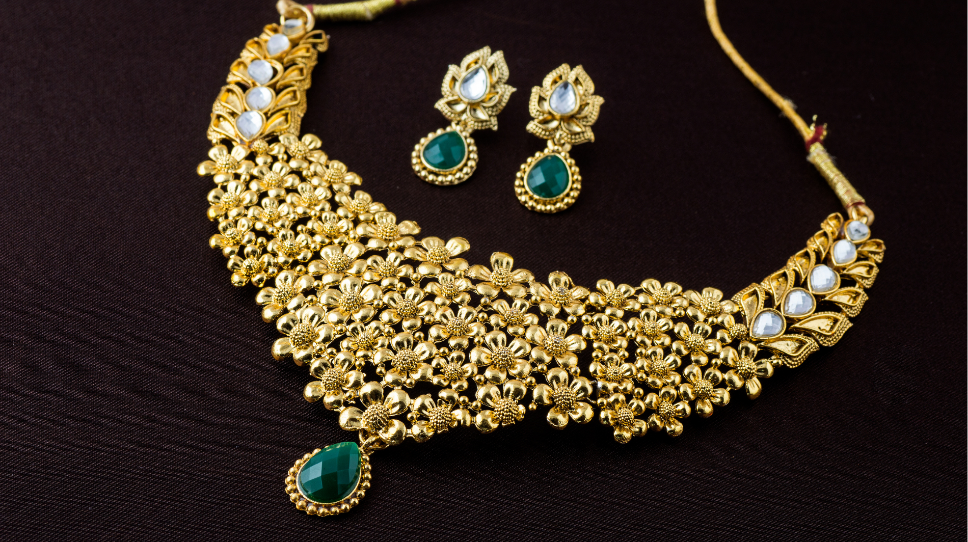 Gold necklace and matching earrings with green gemstones on a dark background
