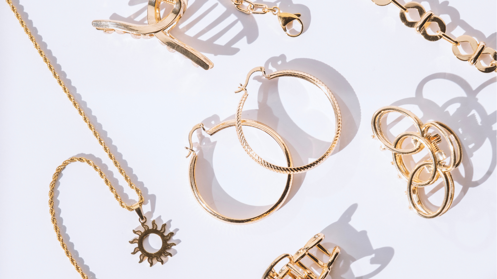 Gold bracelets and earrings arranged on a light background with soft shadows