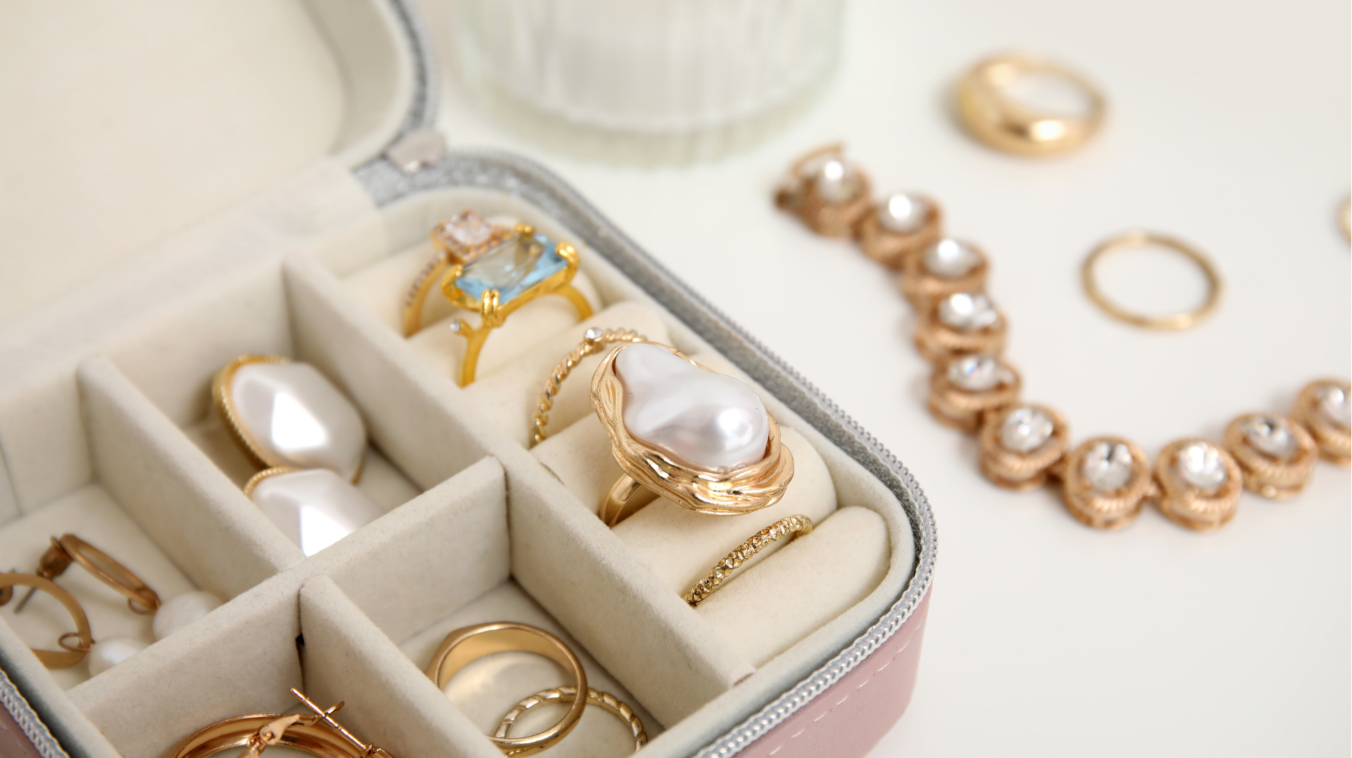 Open jewelry box with rings and pearls beside a pearl necklace on a light surface