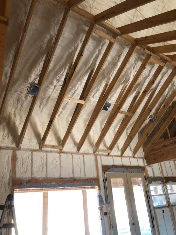 An unfinished room with exposed wooden rafters and walls covered in pale, textured spray foam insulation.